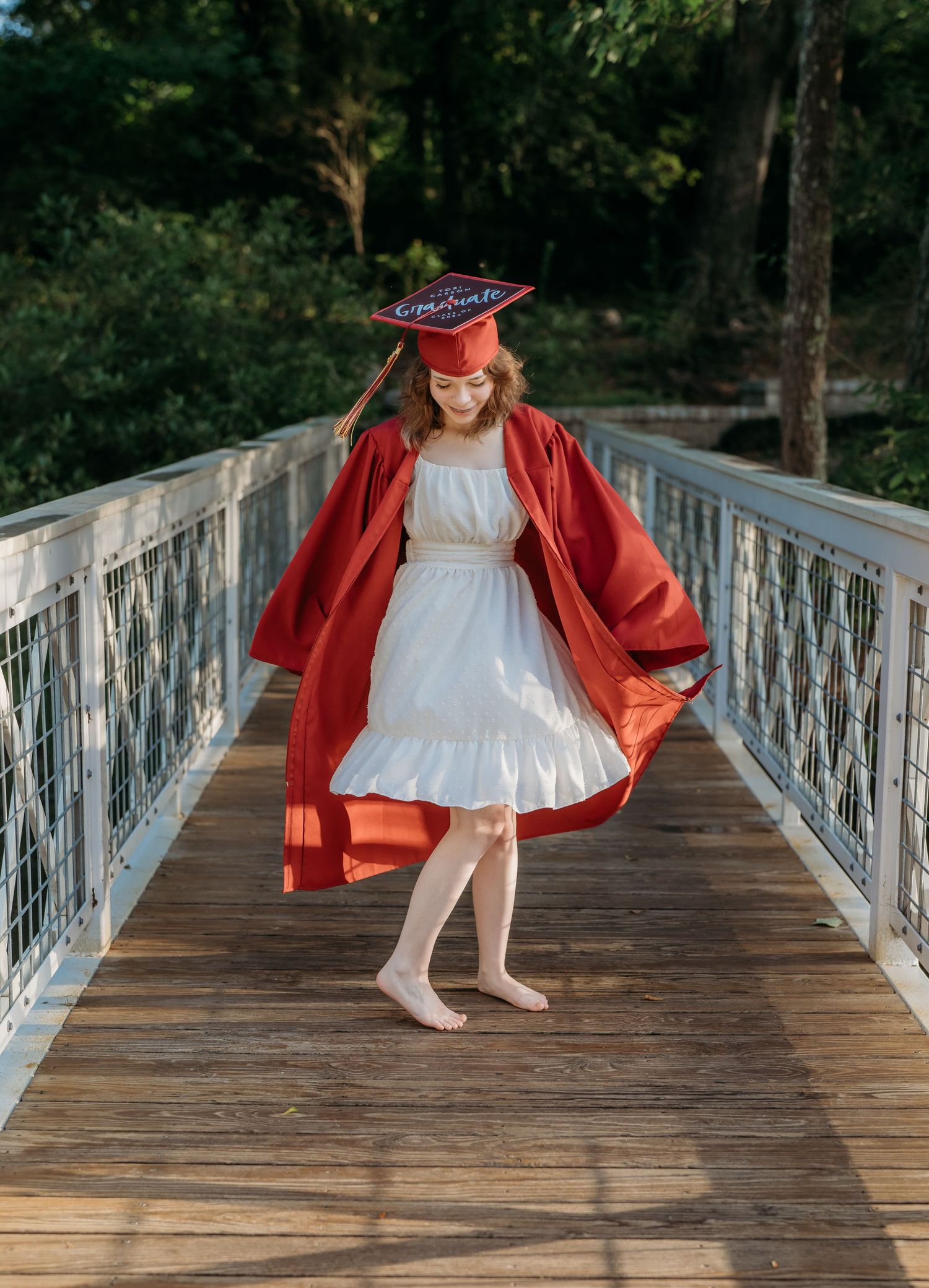 A figure in a red coat and white dress twirls playfully on a wooden bridge surrounded by trees.