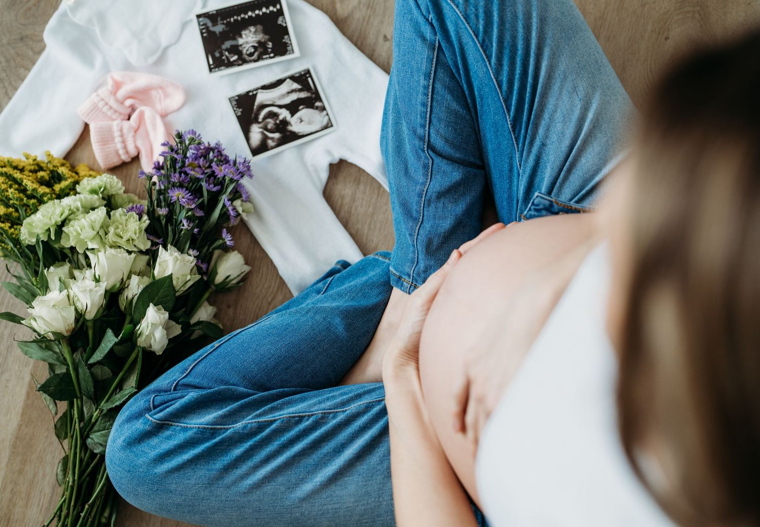 Pregnancy ultrasound photos displayed next to fresh white roses and purple flowers on wooden surface.