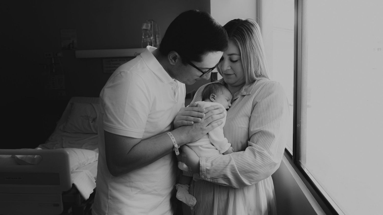 Black and white photo of new parents tenderly holding their newborn baby.