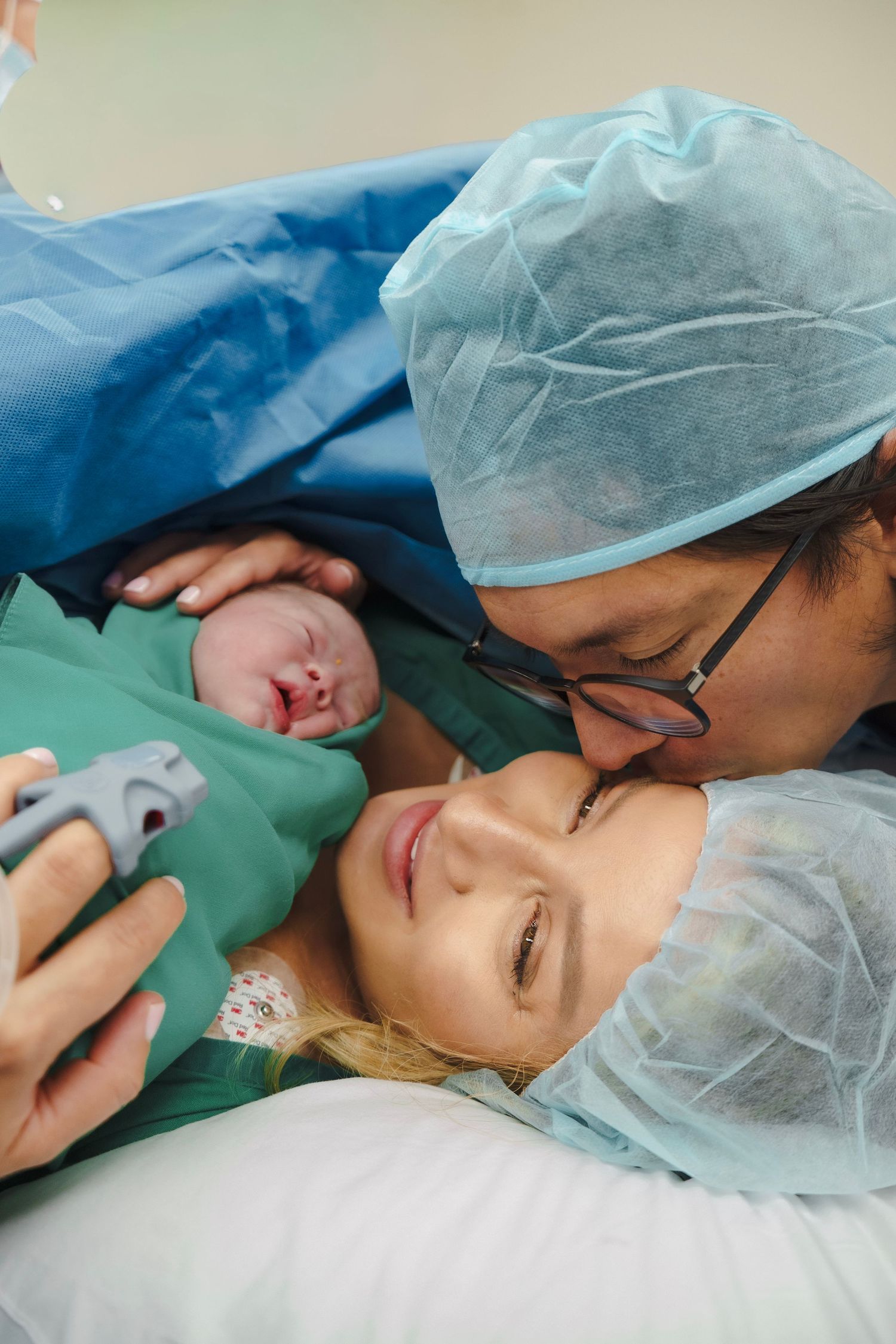 New parents share a tender moment with their newborn baby in a hospital delivery room after a C-section birth.