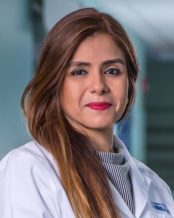Healthcare professional in white coat and striped shirt poses for professional headshot.