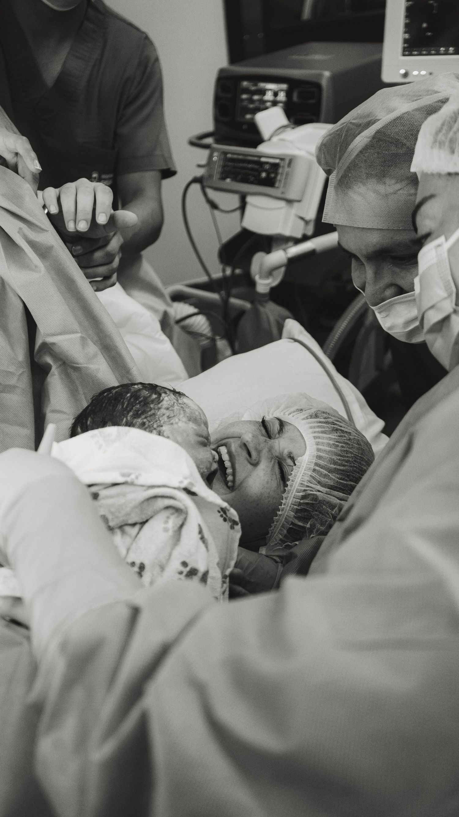 Black and white photo of a mother smiling joyfully as she holds her newborn baby in a hospital delivery room.