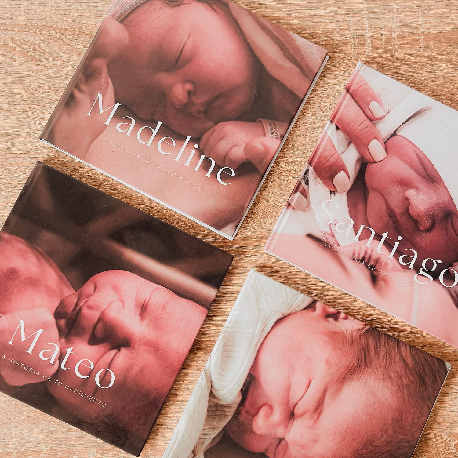 Three personalized newborn photo books named Madeline, Santiago, and Mateo, featuring close-up infant photography on wooden surface.