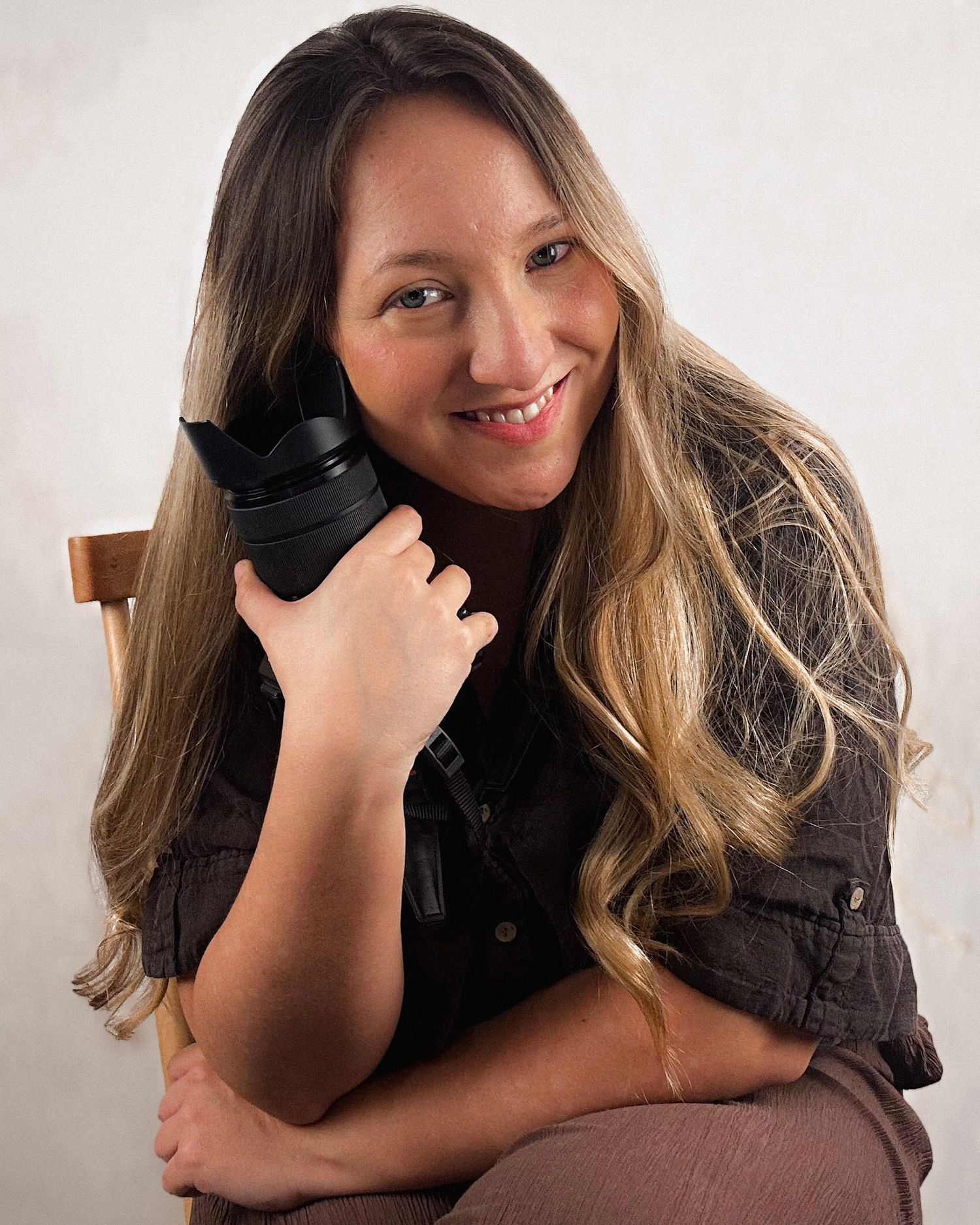Professional photographer in a black shirt holds a camera lens while posing against white background.
