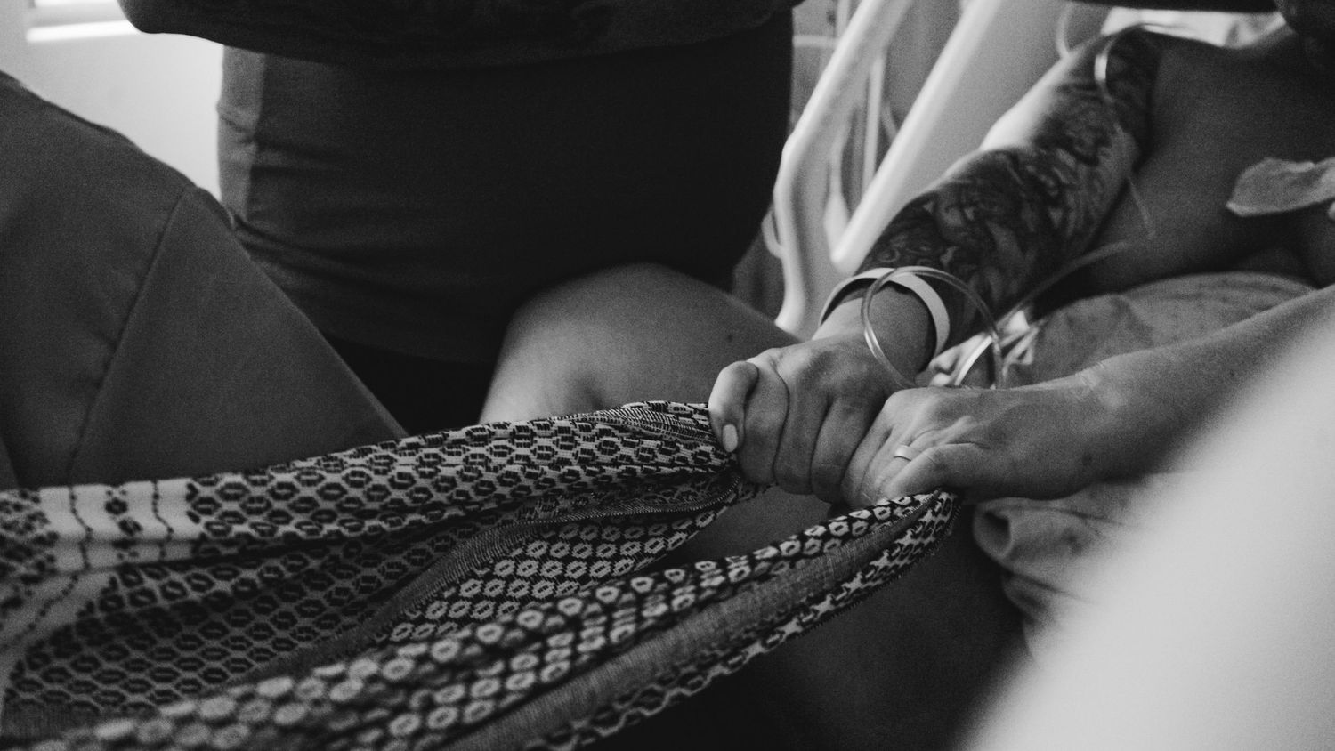 Black and white close-up photograph showing hands working with intricate braided rope or cord material.