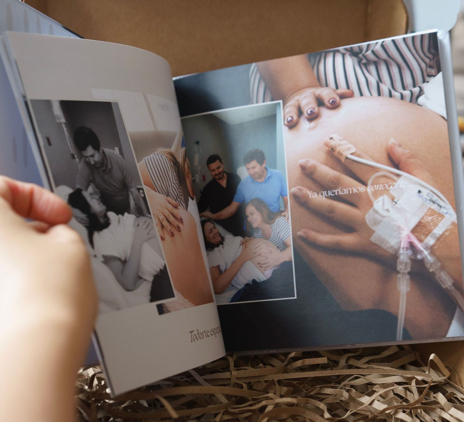 An open photo book displaying pregnancy and family memories, held by a hand, resting on decorative straw.