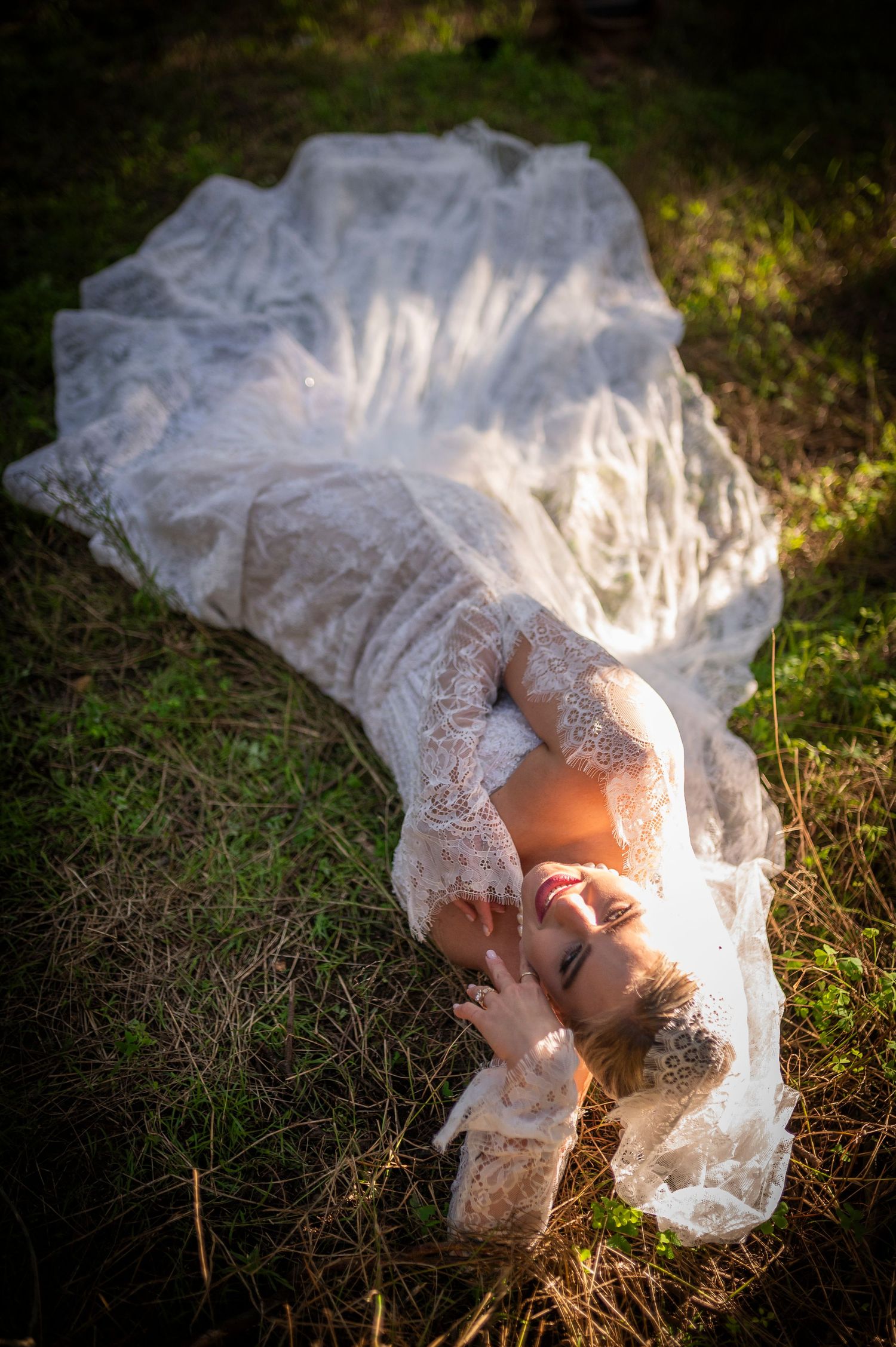 A romantic white lace wedding dress flows across grass in dreamy golden sunlight during an outdoor photo session.