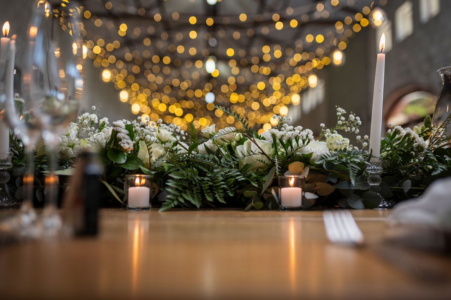 Elegant table setting with candles, greenery and twinkling string lights creating a romantic holiday ambiance.