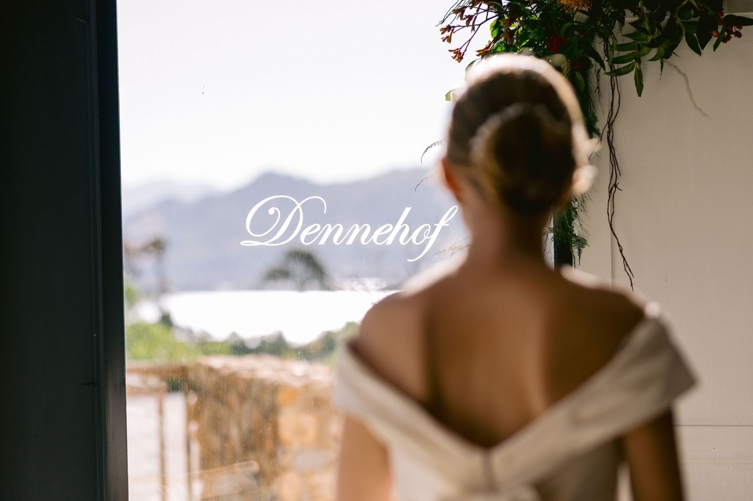 A person in a white wedding dress gazes out at a scenic ocean view from a balcony.
