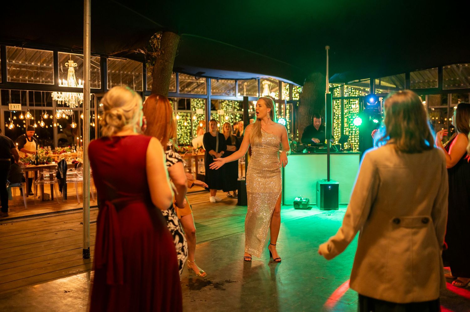 People dance together in a dimly lit venue with green ambient lighting and a festive atmosphere.