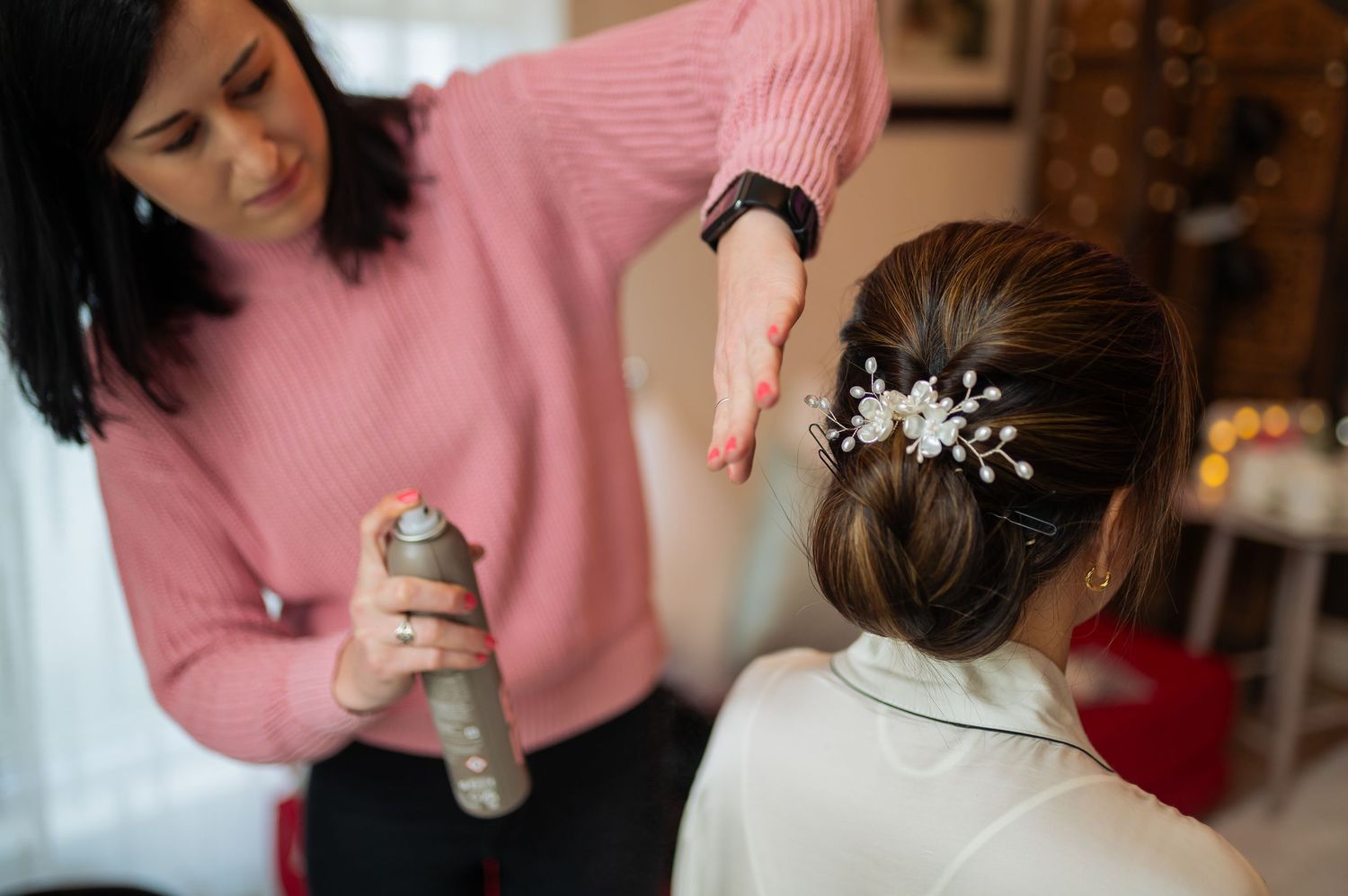 Hairstylist sprays hairspray while styling an elegant updo with crystal hair accessories.