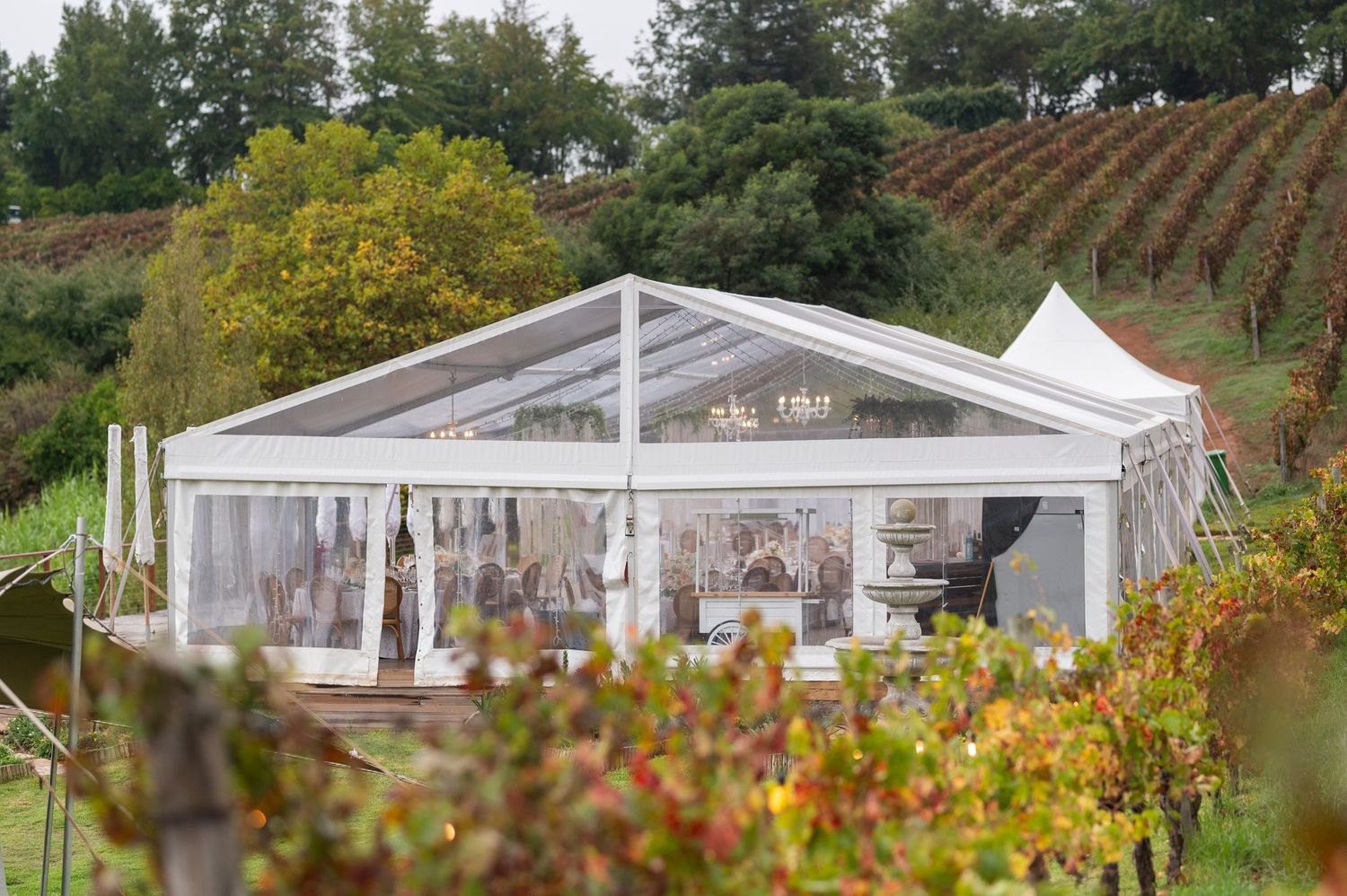 A clear wedding tent pavilion set up in a vineyard with autumn foliage and rolling hills in the background.