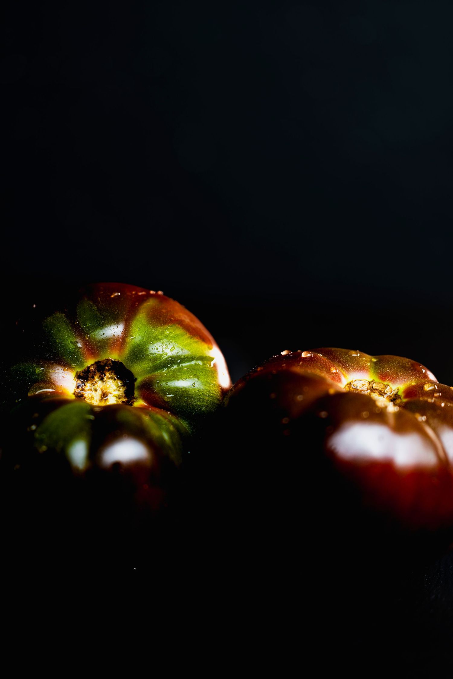 A series of dark artistic photographs showing illuminated tomatoes with dramatic lighting and shadows against black backgrounds.