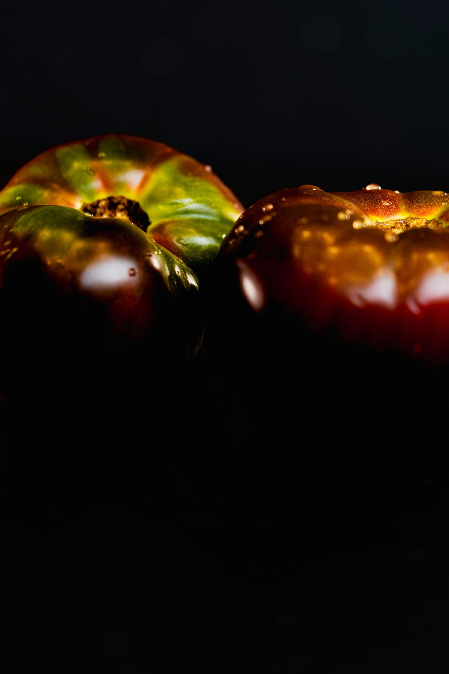 Dark food photography with heirloom tomatoes showing glossy surfaces and rich colors against black background.
