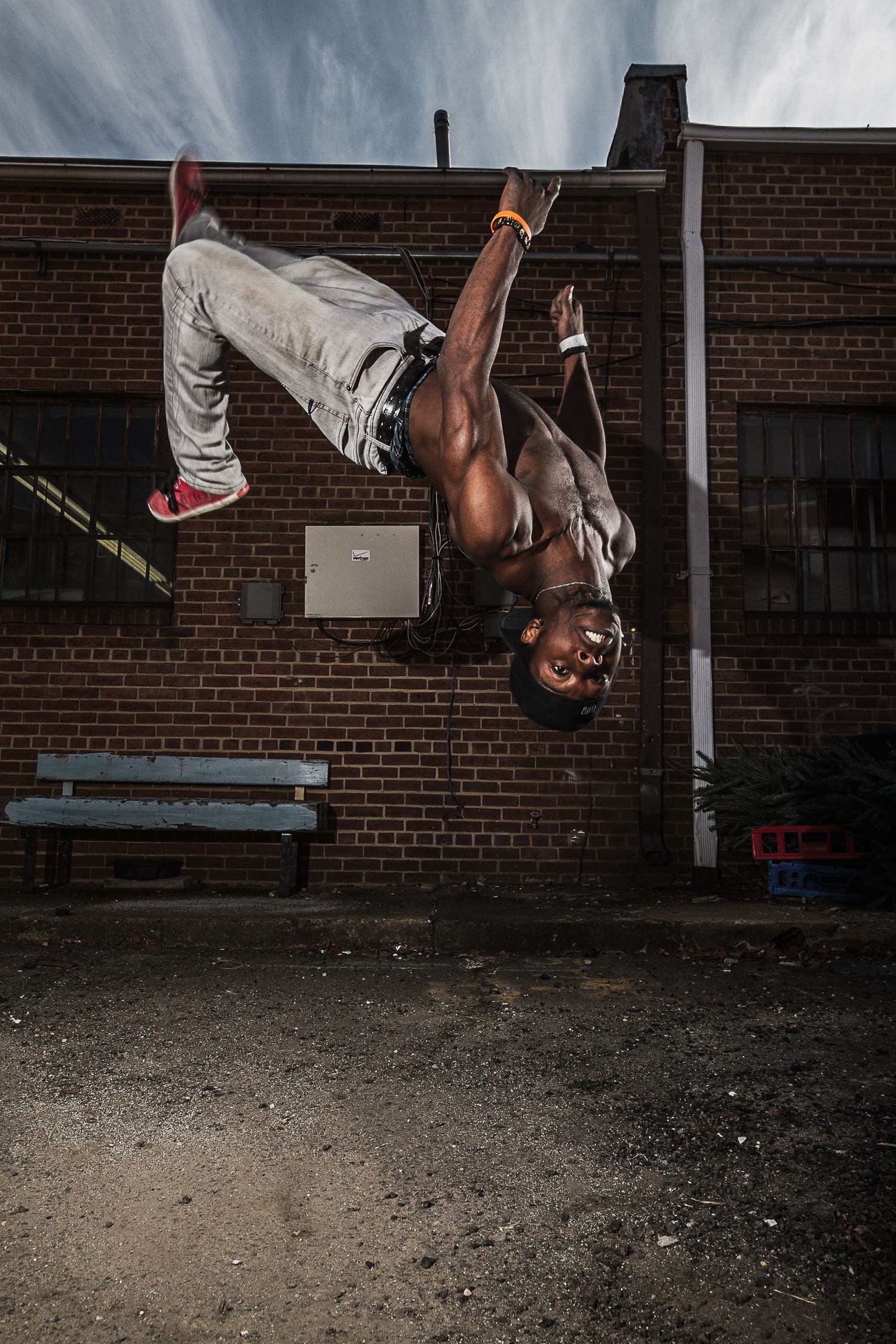 Athletic performer executes an impressive inverted hip-hop dance move against a brick wall backdrop in an urban setting.