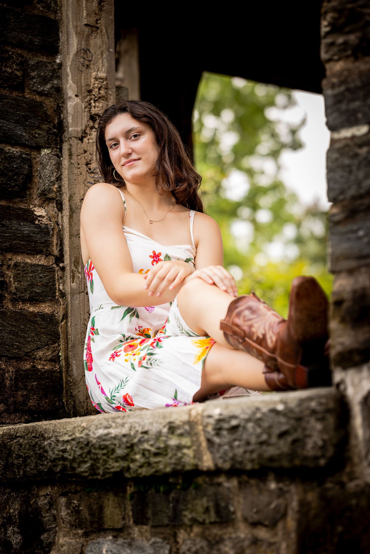 A floral sundress and brown boots complement the rustic stone architecture in this charming outdoor portrait.