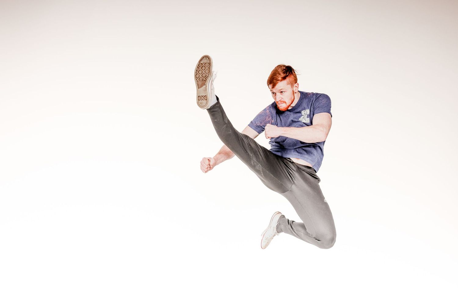 Dancer in gray pants performs a dynamic high kick against a white background.