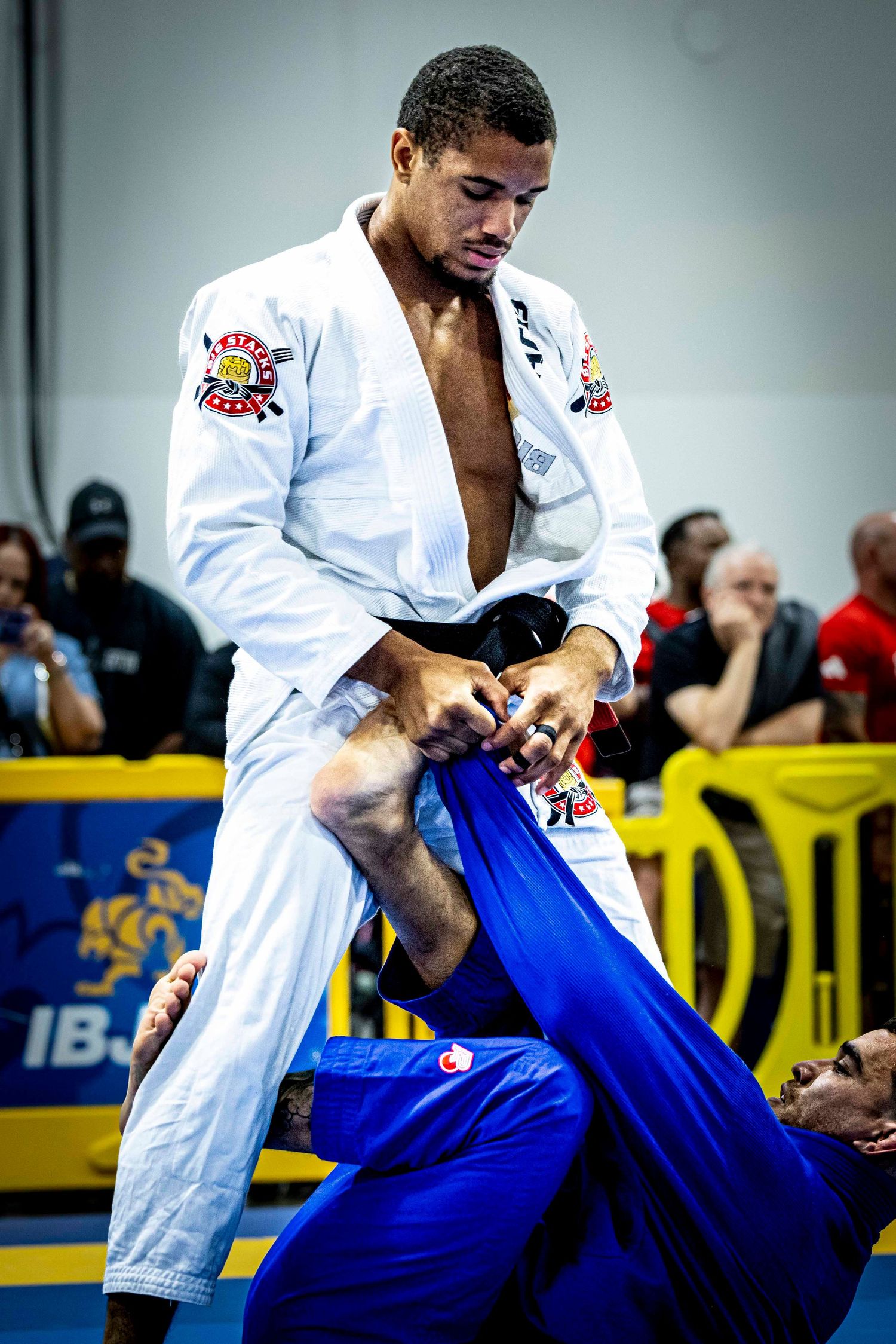 Brazilian Jiu-Jitsu competitor in white gi executing a guard pass technique during tournament match.