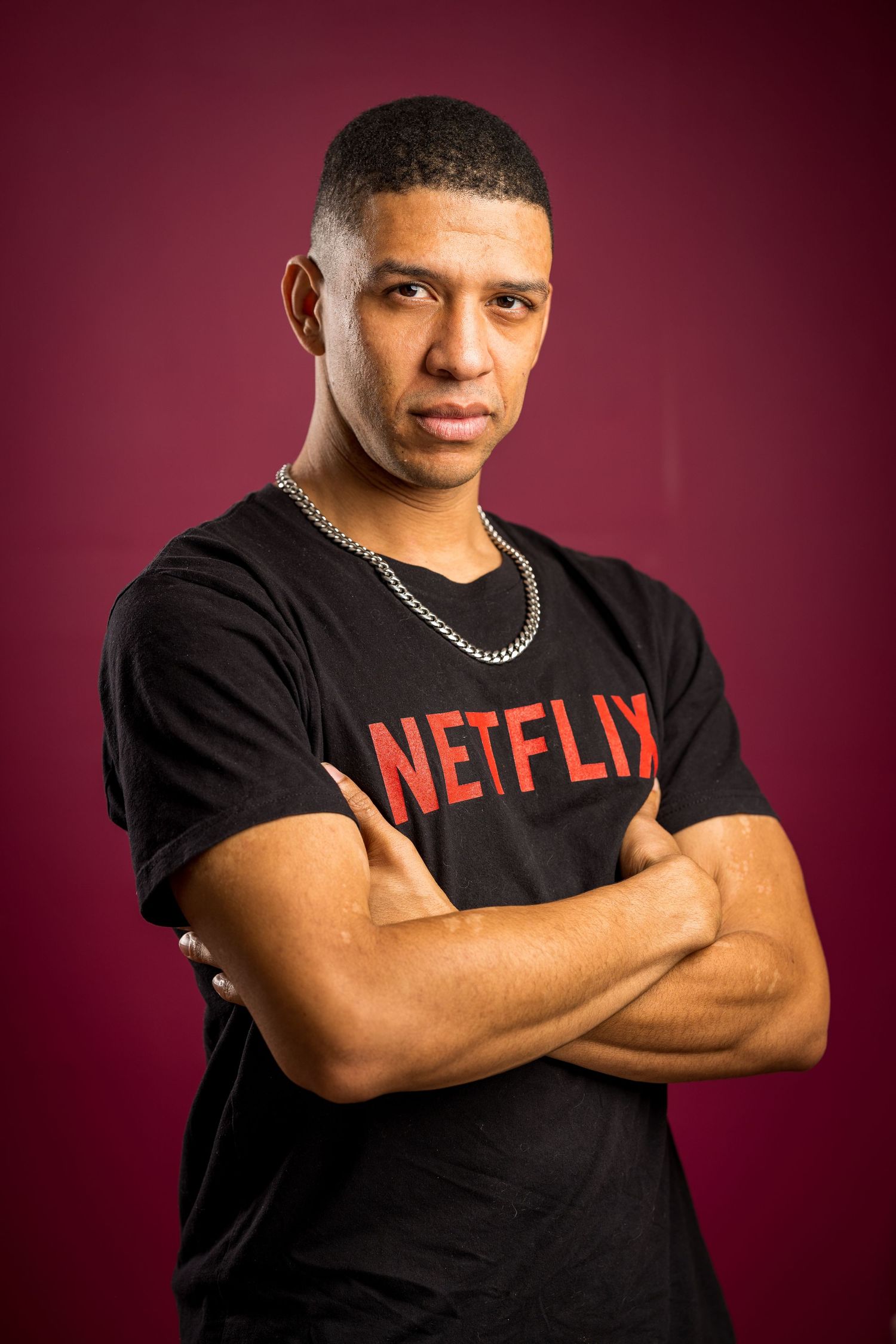 Studio portrait of someone wearing a black Netflix t-shirt and silver chain against a burgundy background.