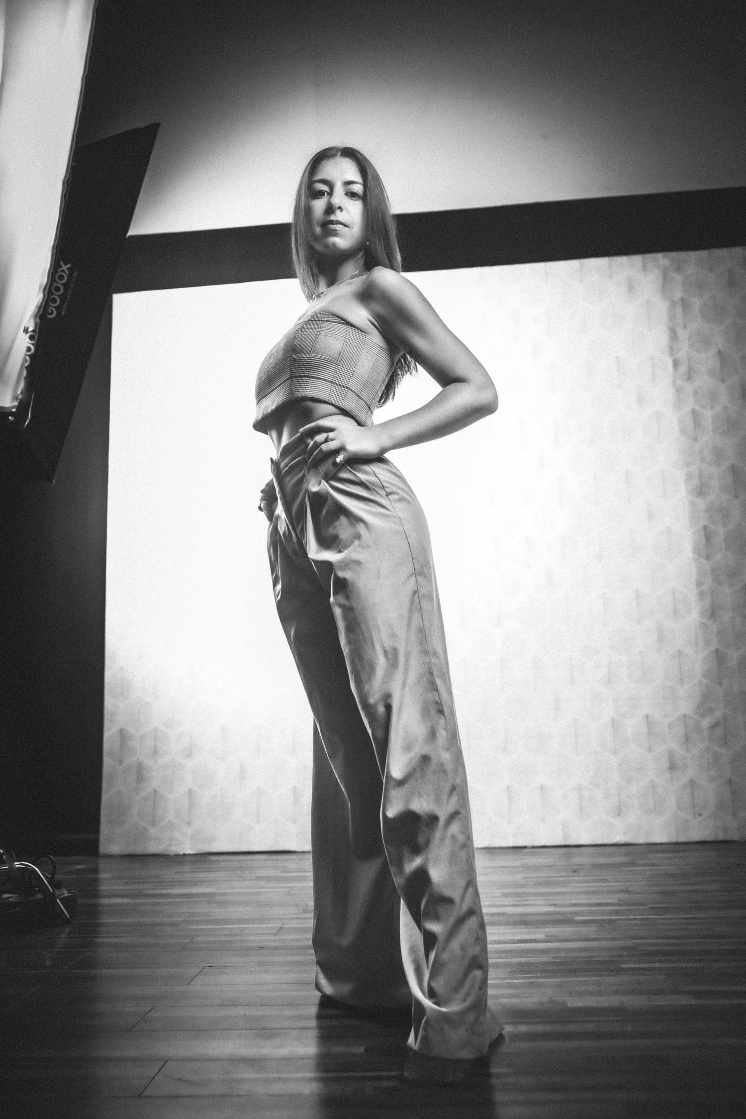 Dramatic black and white fashion photo showing model in crop top and wide-leg pants posing on wooden floor.
