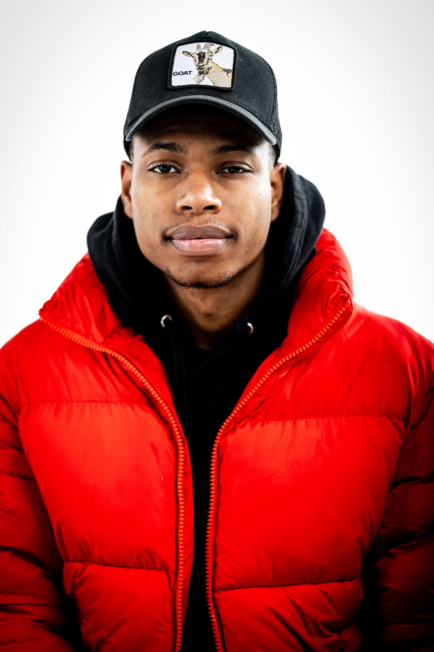 Portrait of someone in a bright red puffer jacket and black baseball cap against a white backdrop.