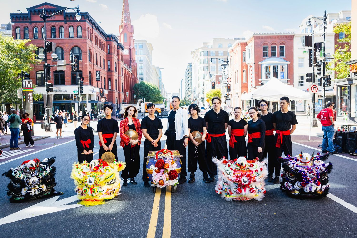Performers in traditional costumes pose with colorful lion dance props on a Boston city street with historic buildings.