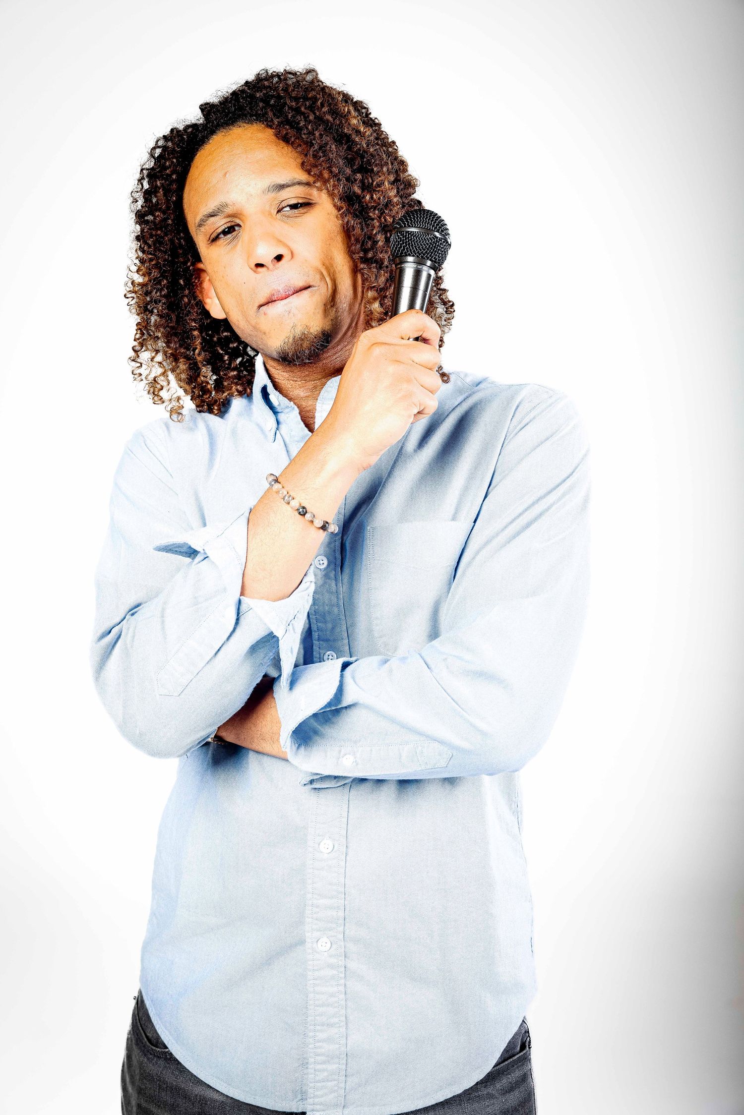 Person with curly hair holding microphone while wearing light blue button-up shirt.