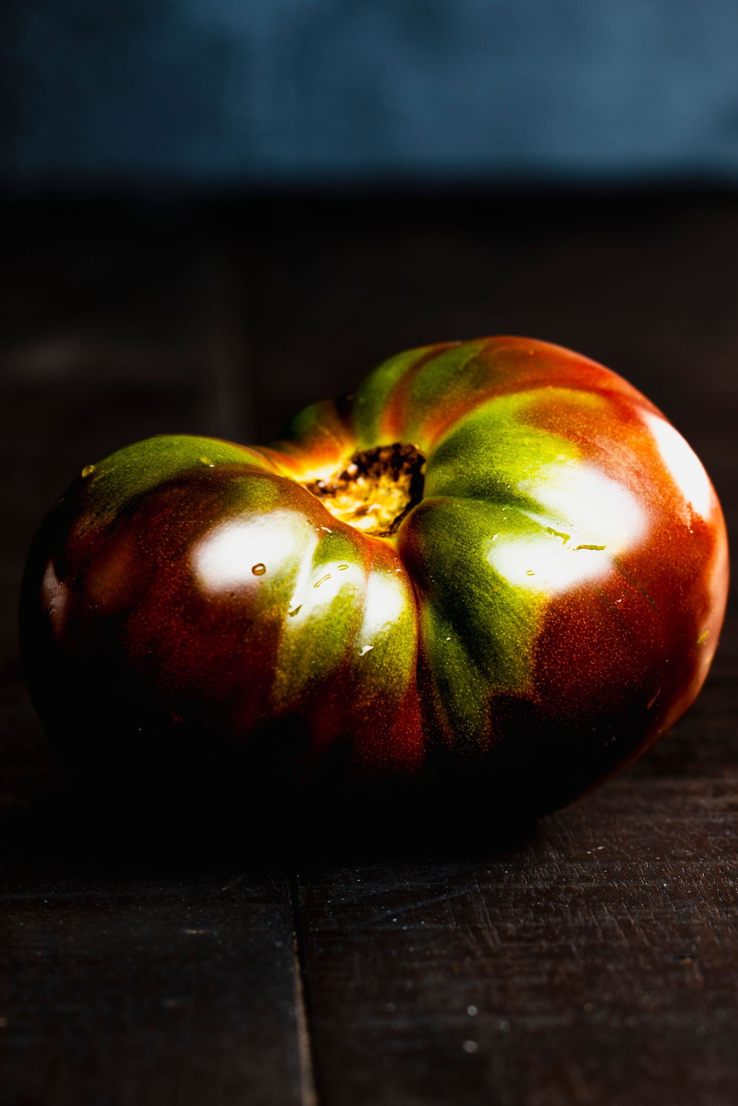 A series of fresh heirloom tomatoes on a dark background with dramatic side lighting creating a moody atmosphere.