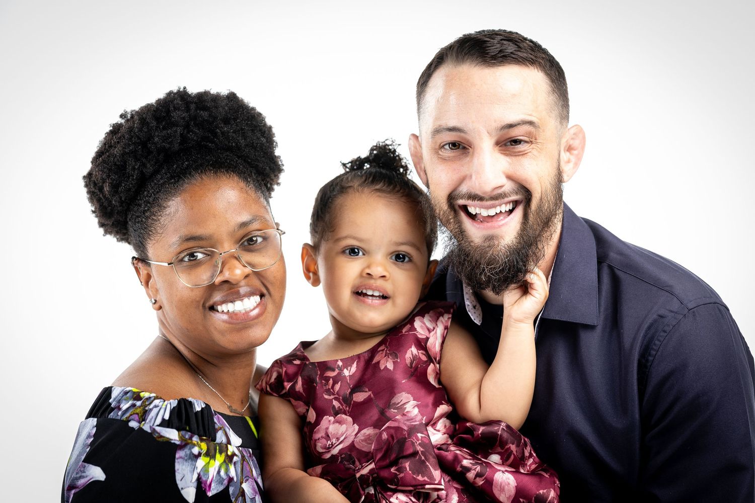 A happy family of three poses together for a professional studio portrait against a light gray background.