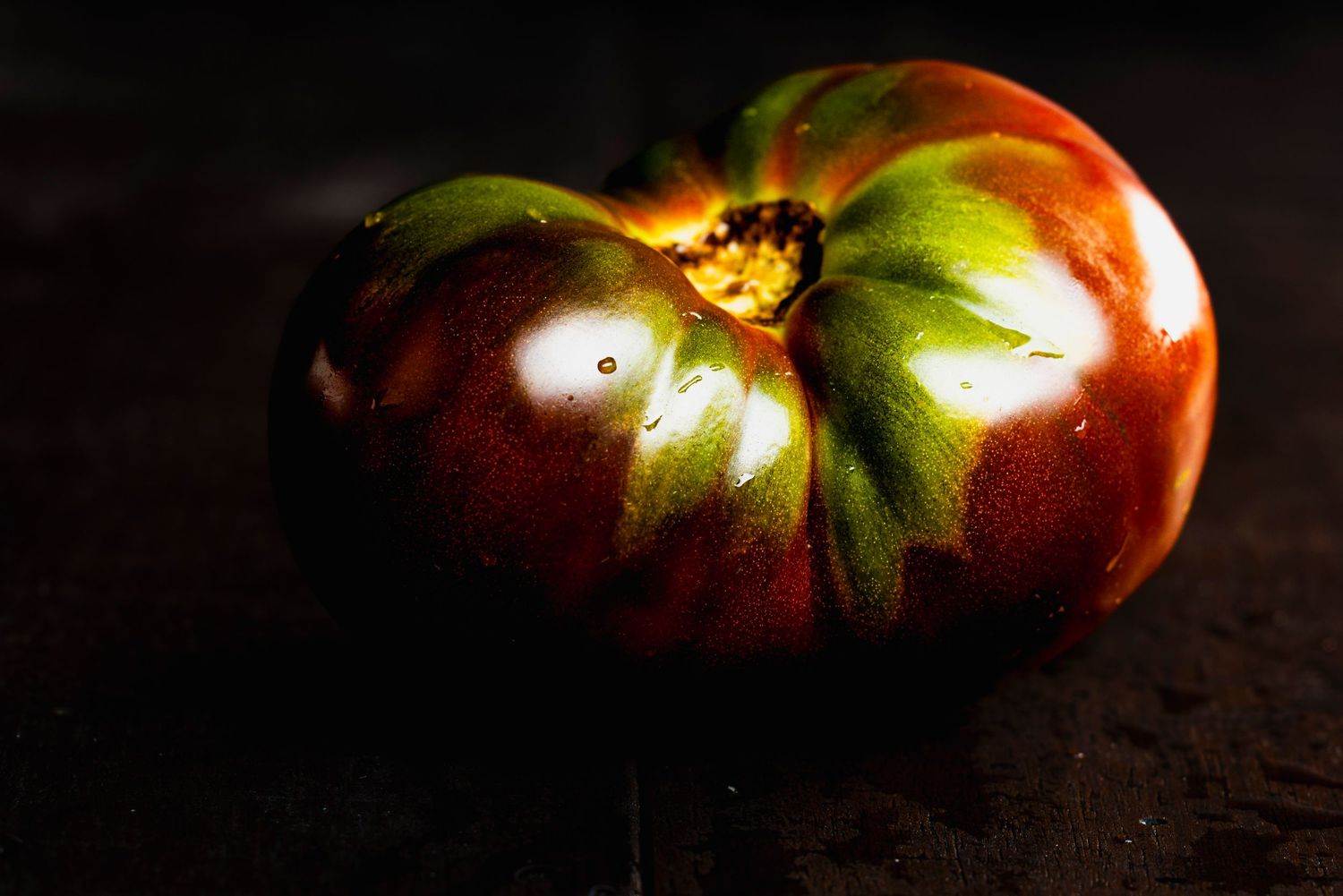 Ripe heirloom tomatoes with varied colors and textures displayed dramatically on dark surface with moody lighting.