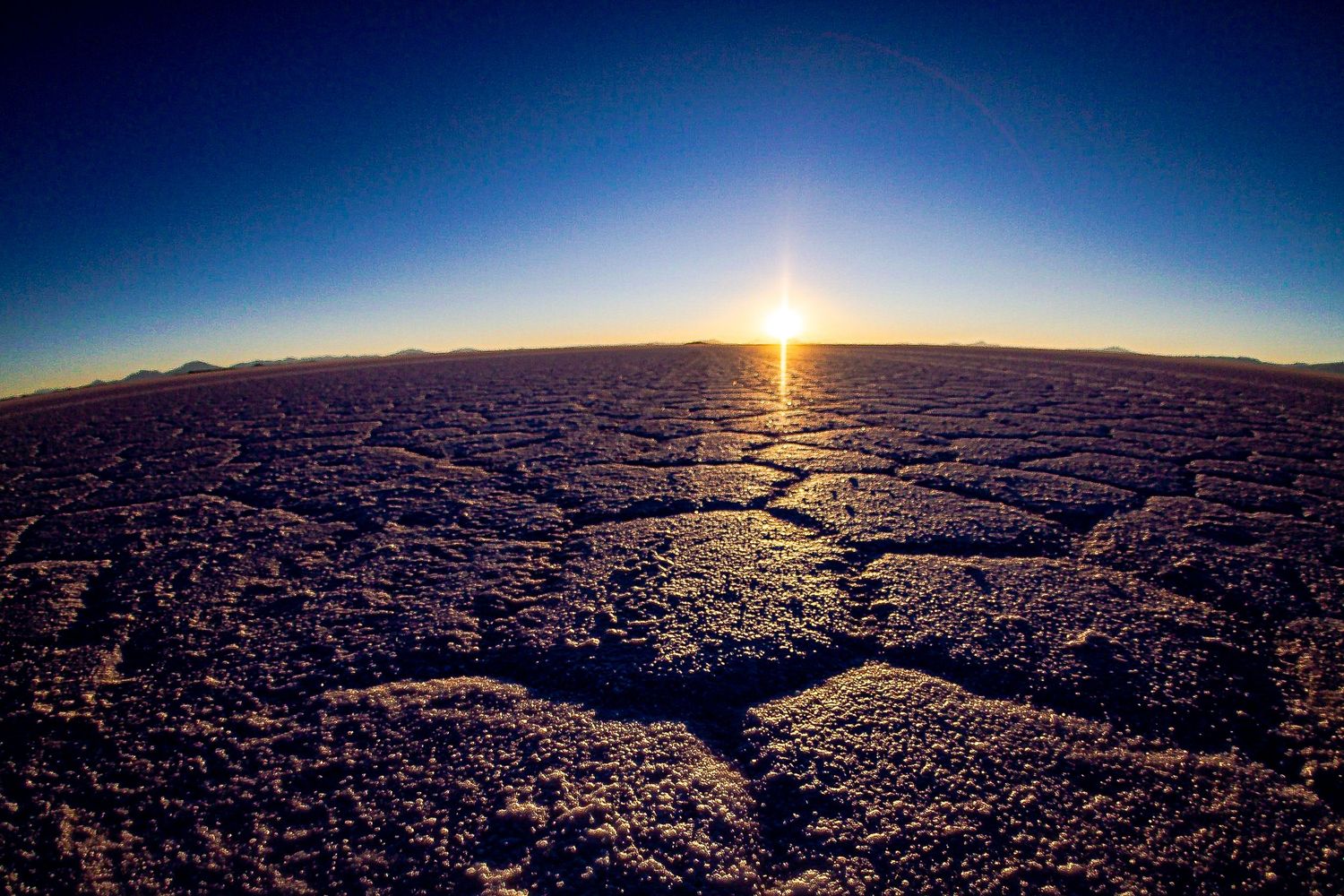 Dramatic sunset over cracked desert terrain with dark blue sky.