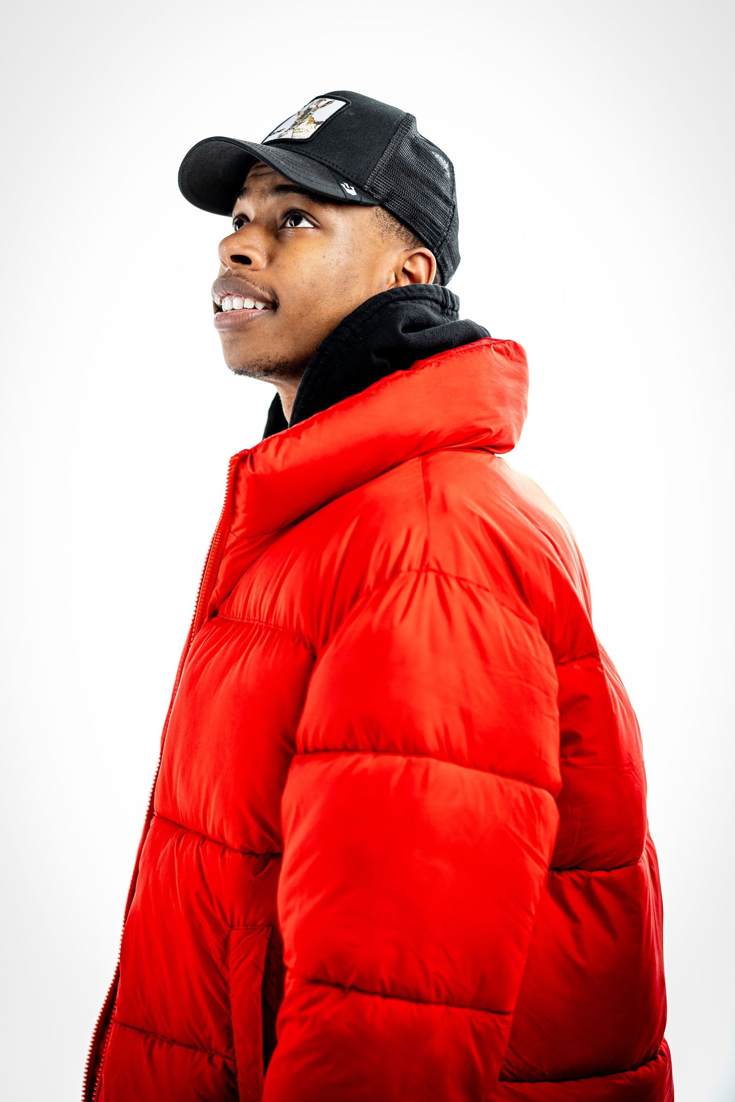 Fashion portrait of person in red puffer jacket and black cap against white background.