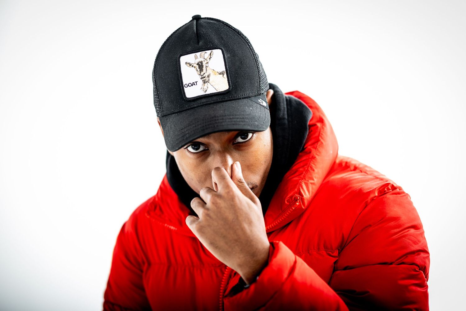 Person in a red puffer jacket and black baseball cap covering their face against white background.