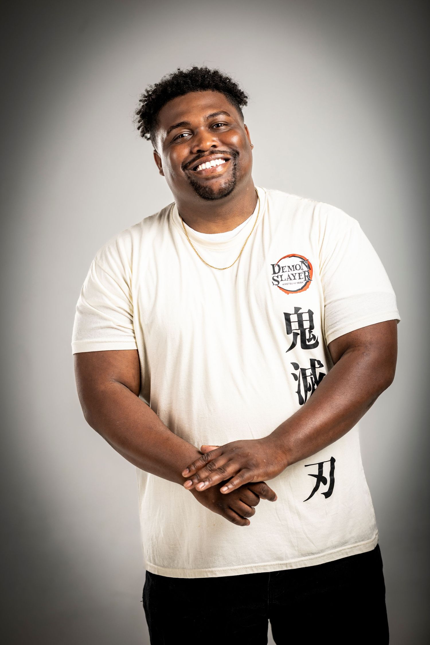 A cheerful person wearing a white t-shirt with Japanese characters stands against a gray background.