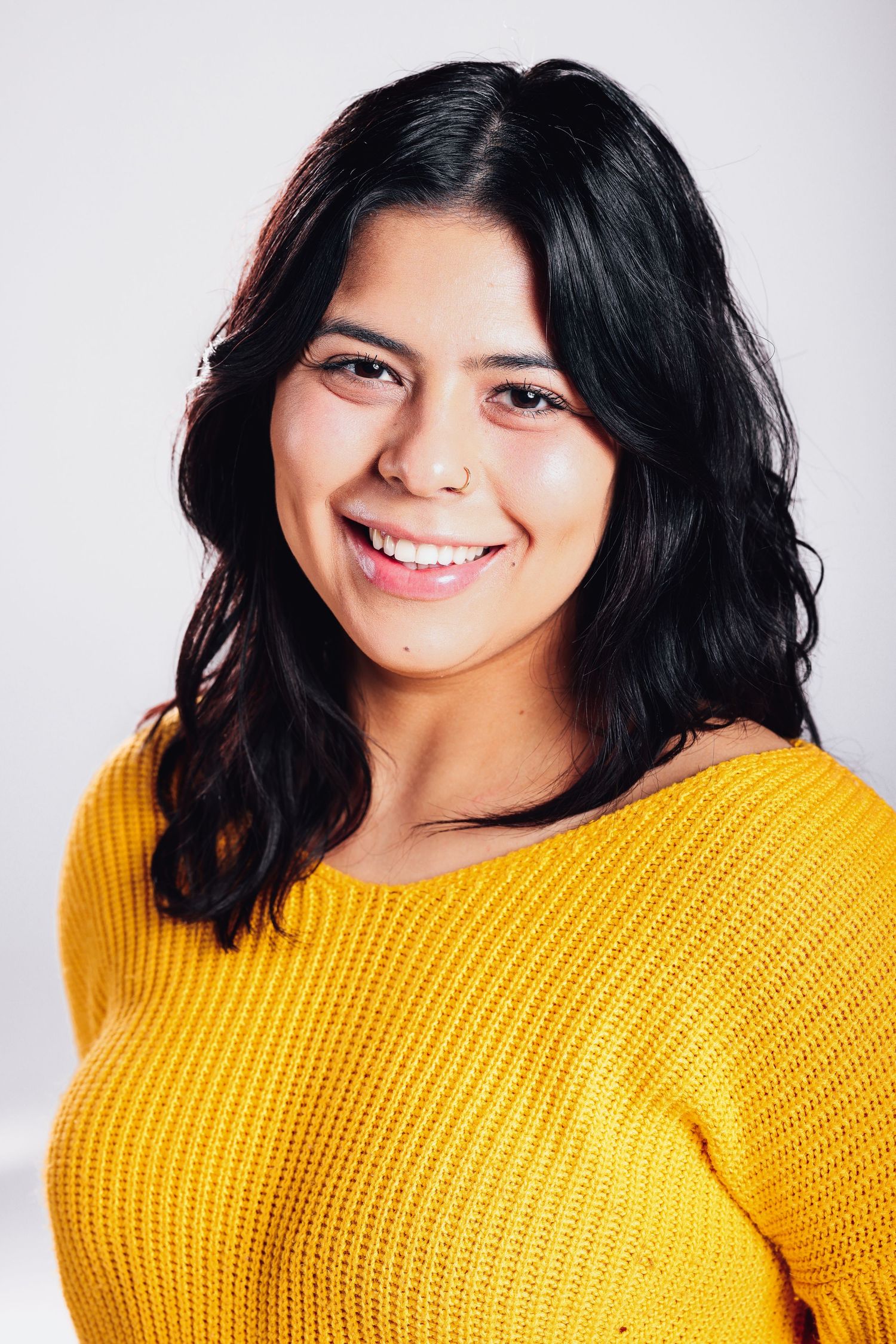 A person in a yellow knit sweater smiles warmly against a light background.