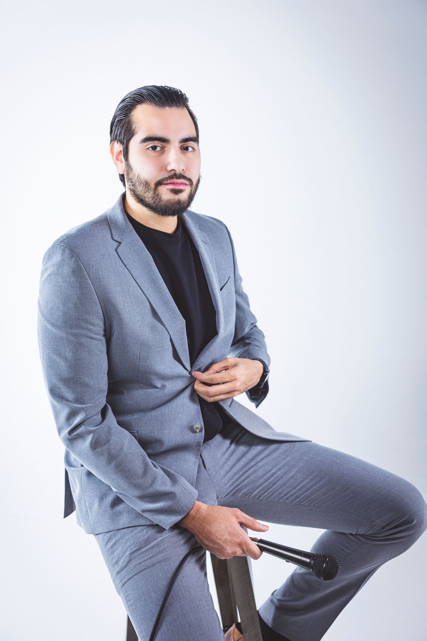 Professional portrait of person in grey suit sitting confidently against light background.