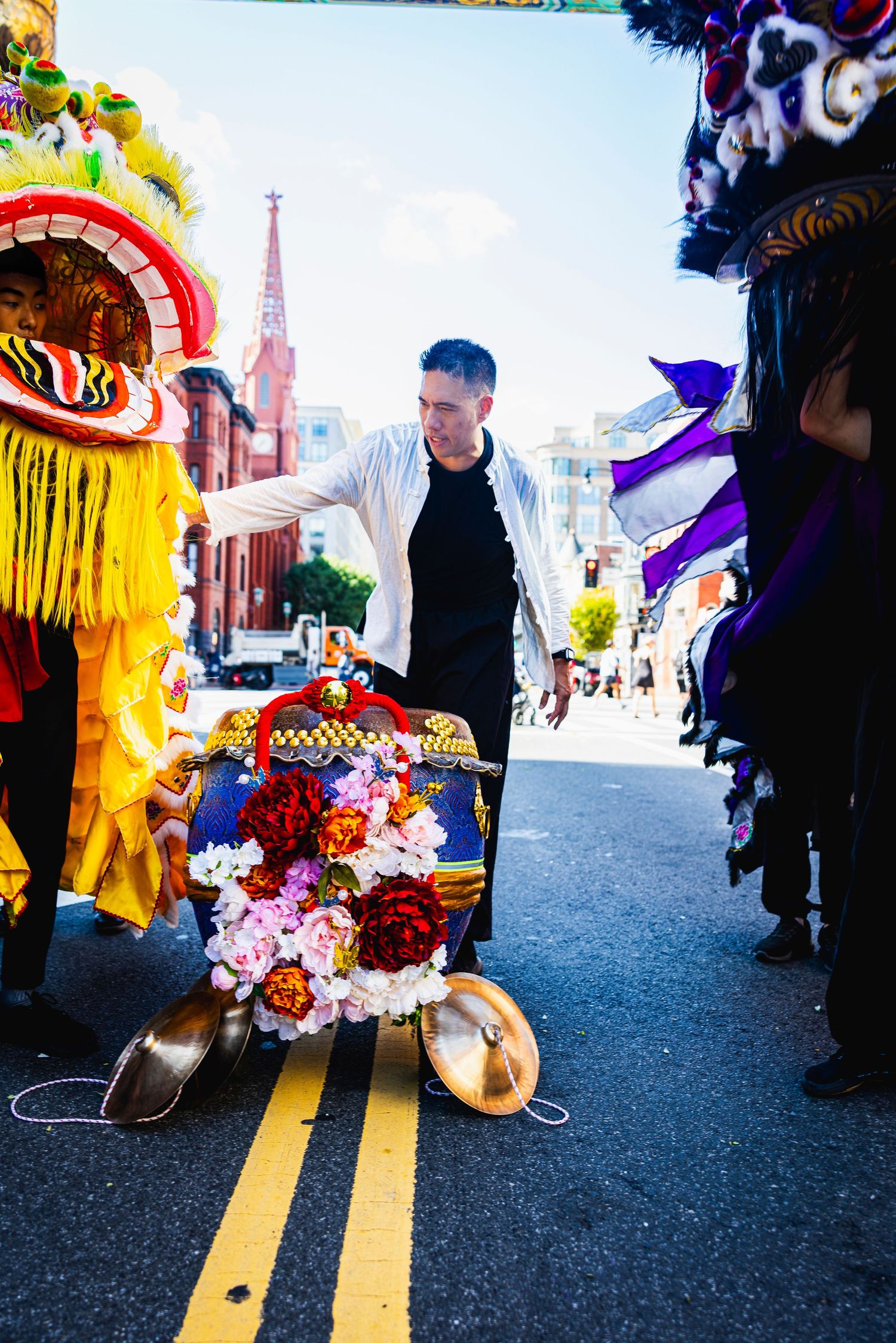 Colorful Chinese dragon dancers perform at a street festival with traditional costumes and floral decorations on the pavement.