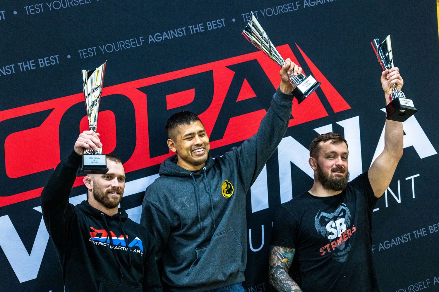 Three competitors on stage holding up trophies and celebrating during a sports or gaming tournament event.
