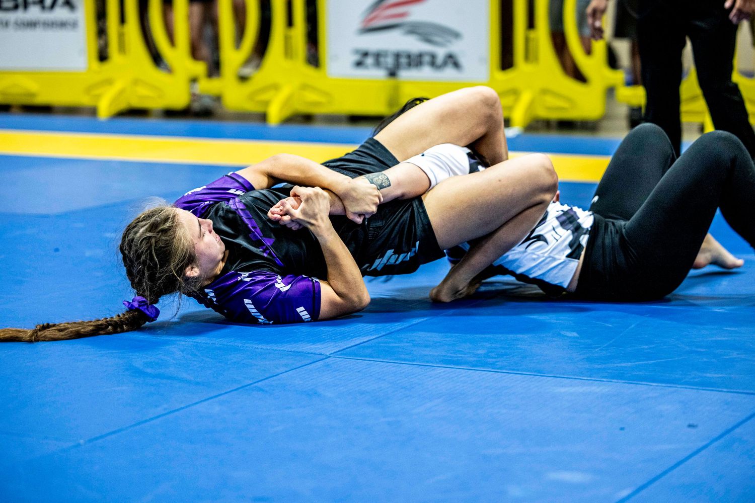 Two competitors grappling intensely on blue competition mats during BJJ tournament.