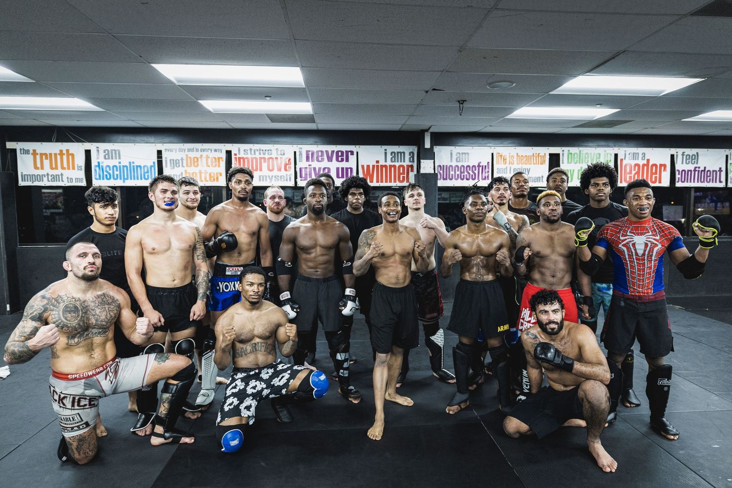 Mixed martial arts fighters and training partners pose together at a combat sports gym after a workout session.