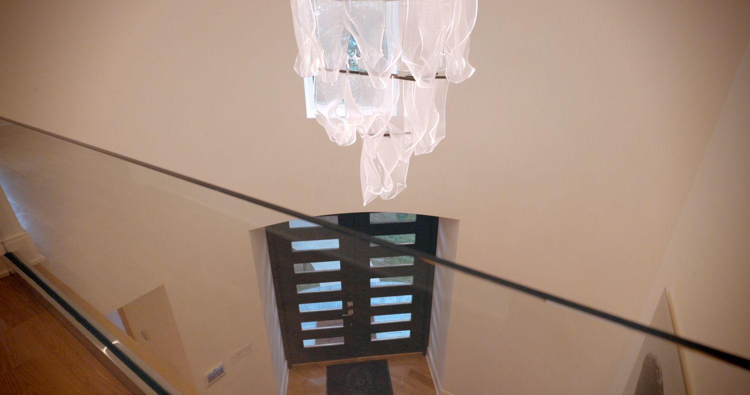 Six square light fixtures mounted on a ceiling track illuminate a modern white interior space with clean lines.