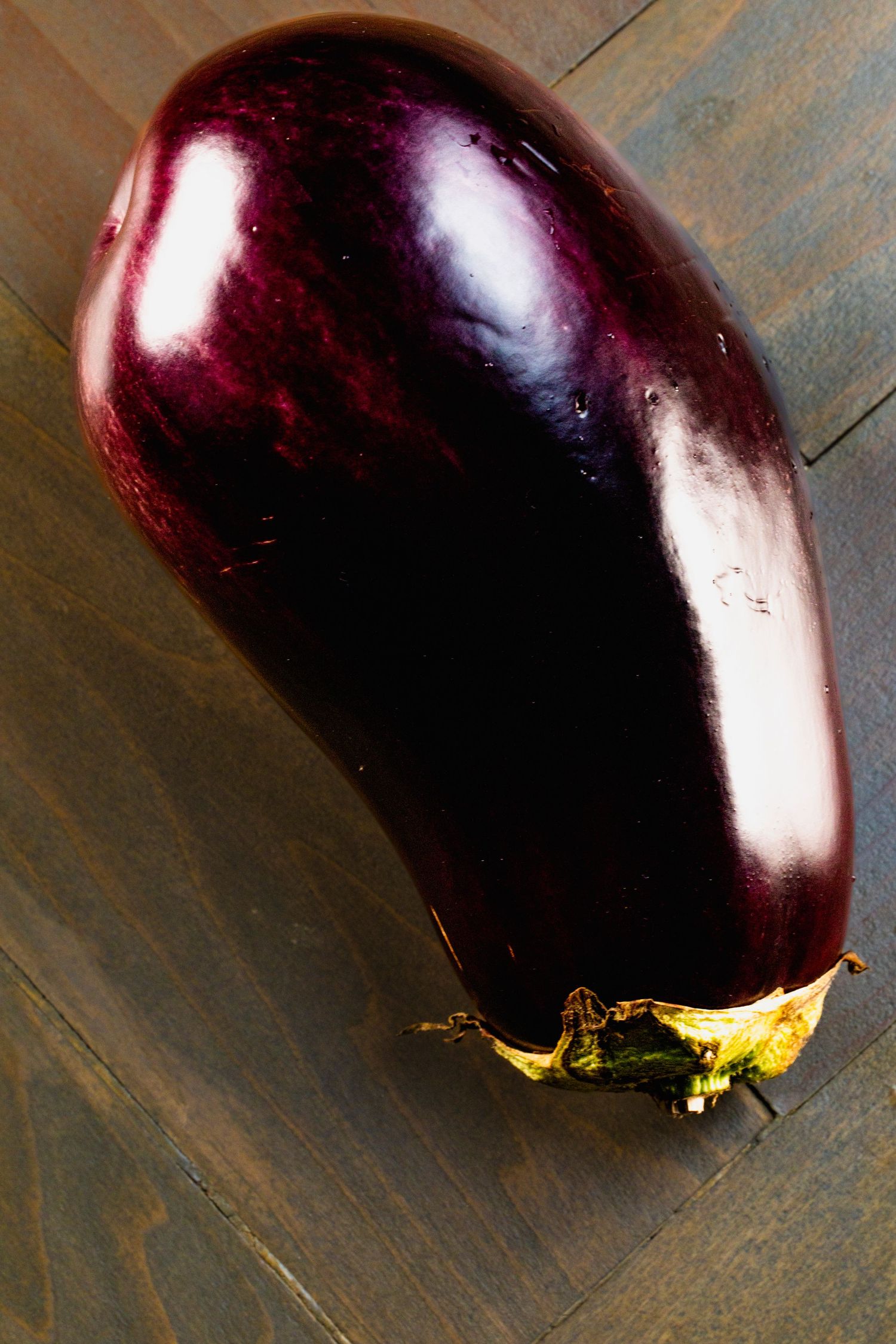 Large ripe purple eggplant on wooden surface with dramatic lighting.