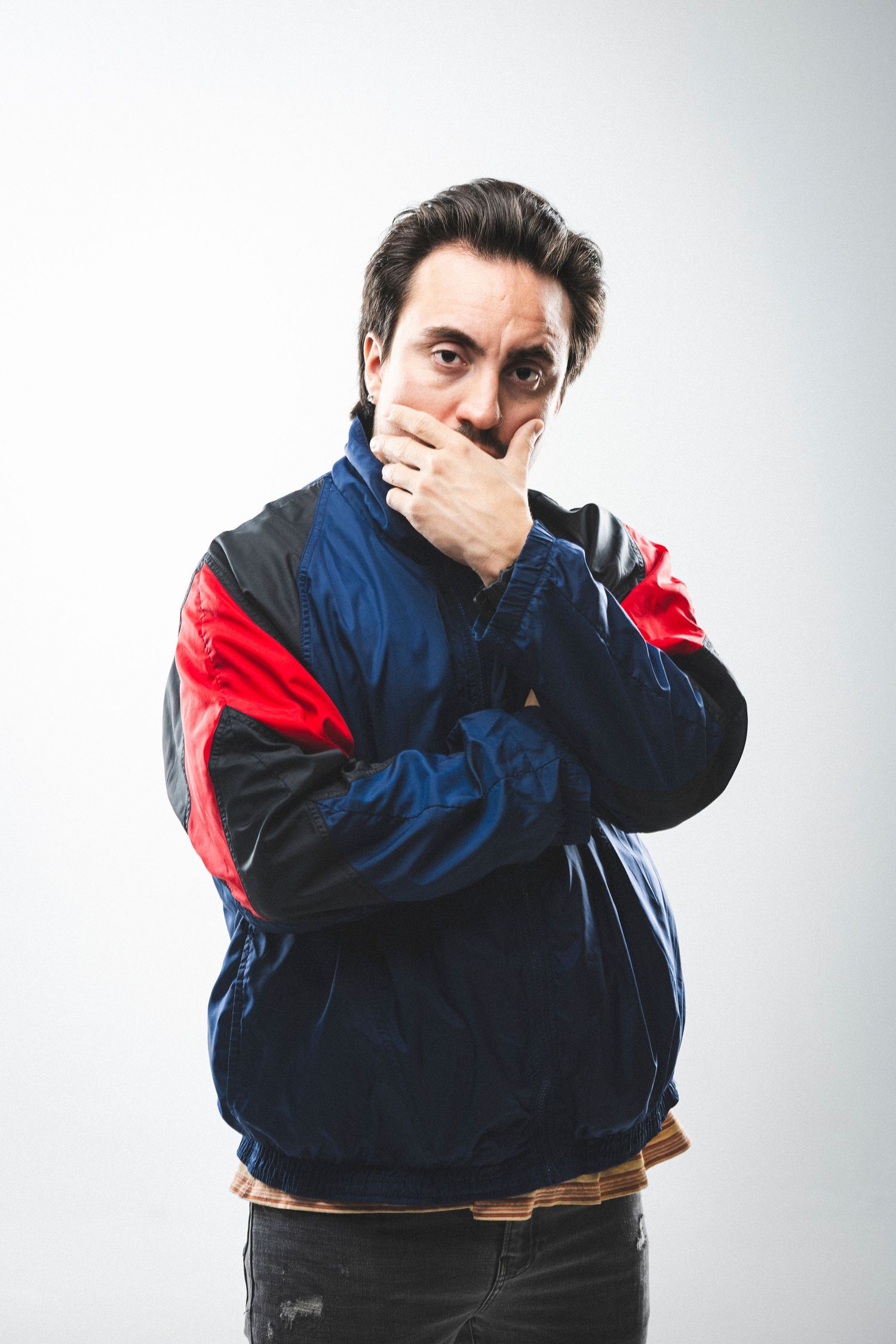Person in blue and red windbreaker jacket covering mouth with surprised expression.