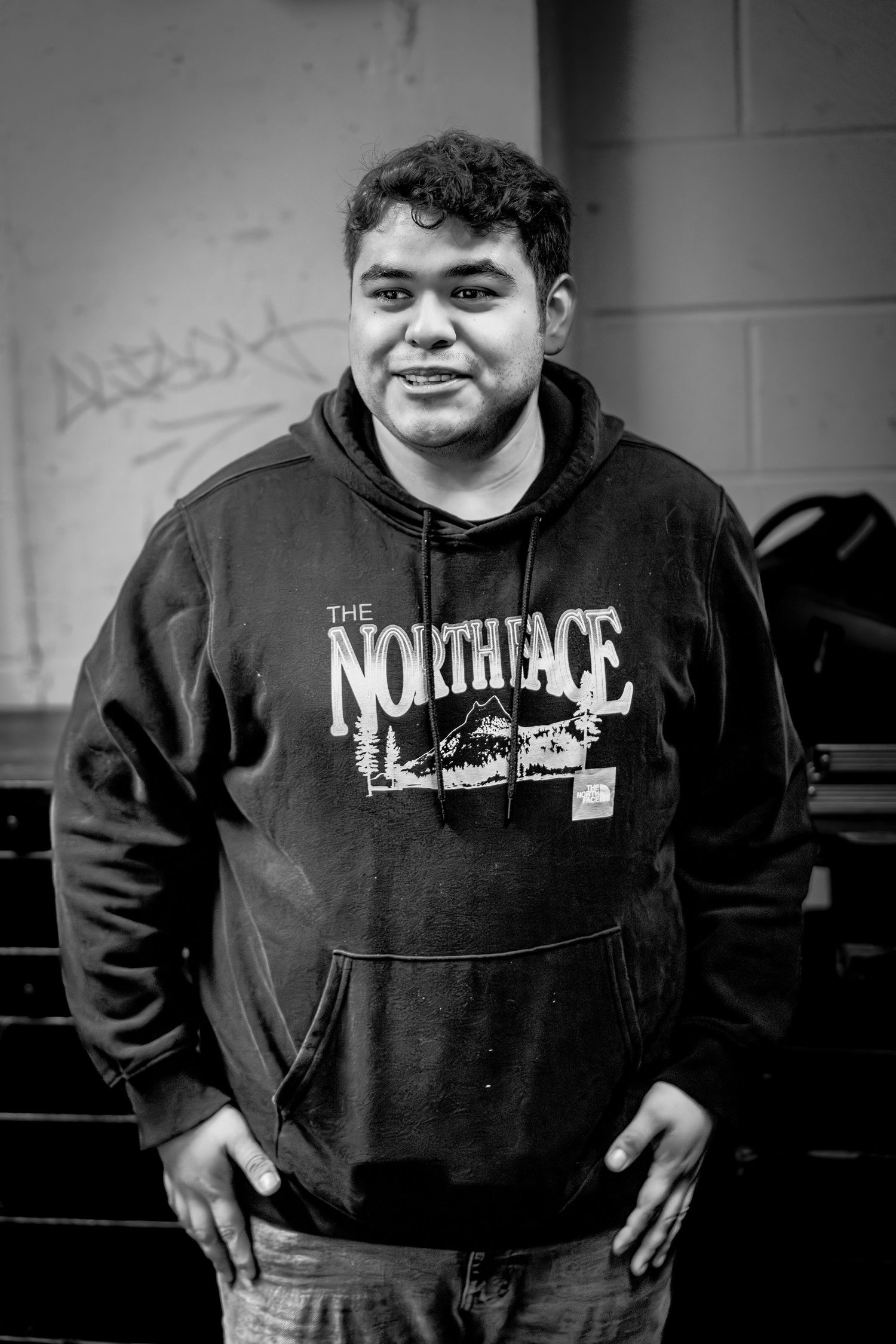 Black and white portrait of someone wearing a North Face hoodie standing against a wall in casual pose.