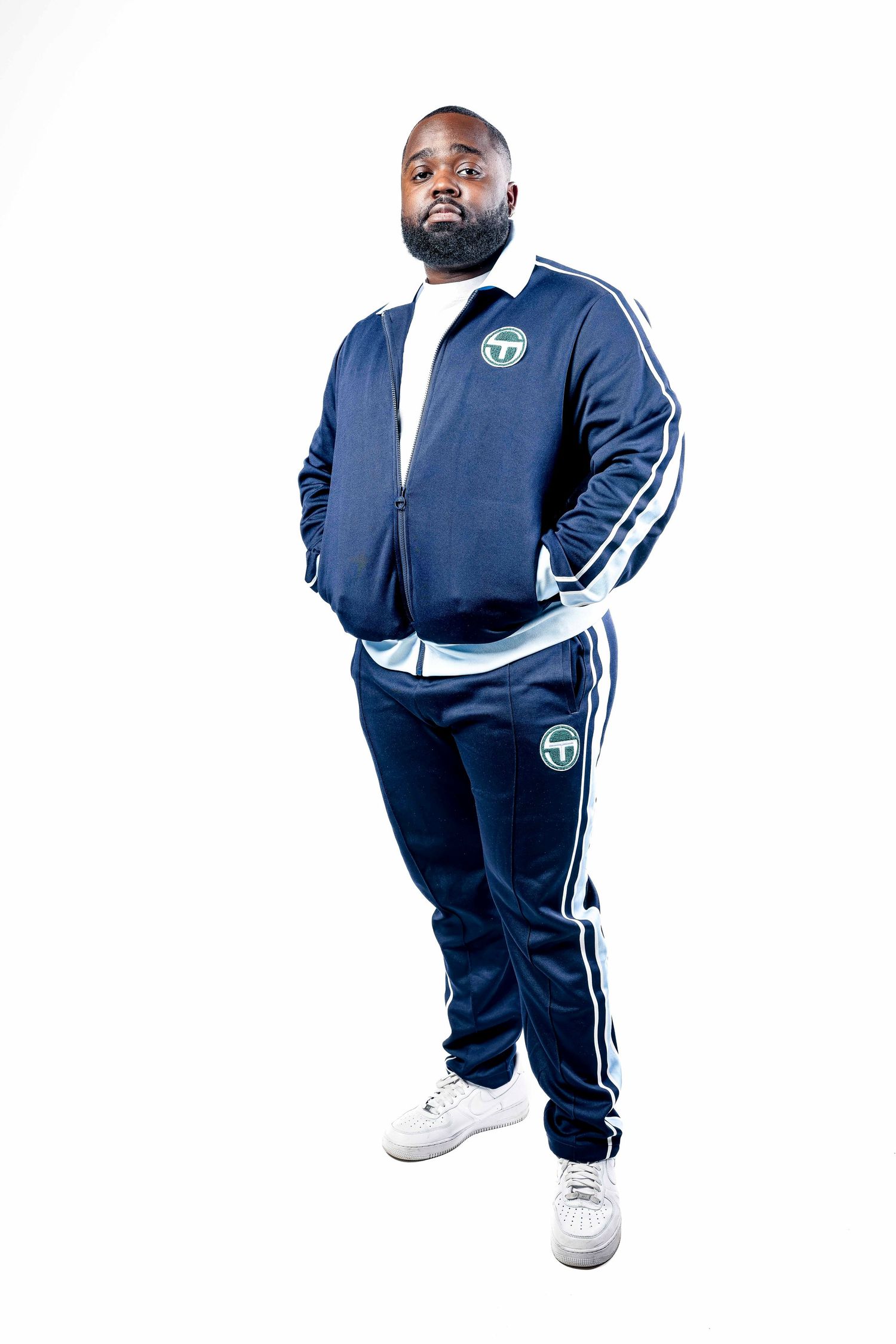 Person wearing blue tracksuit with white stripes standing confidently against white background.