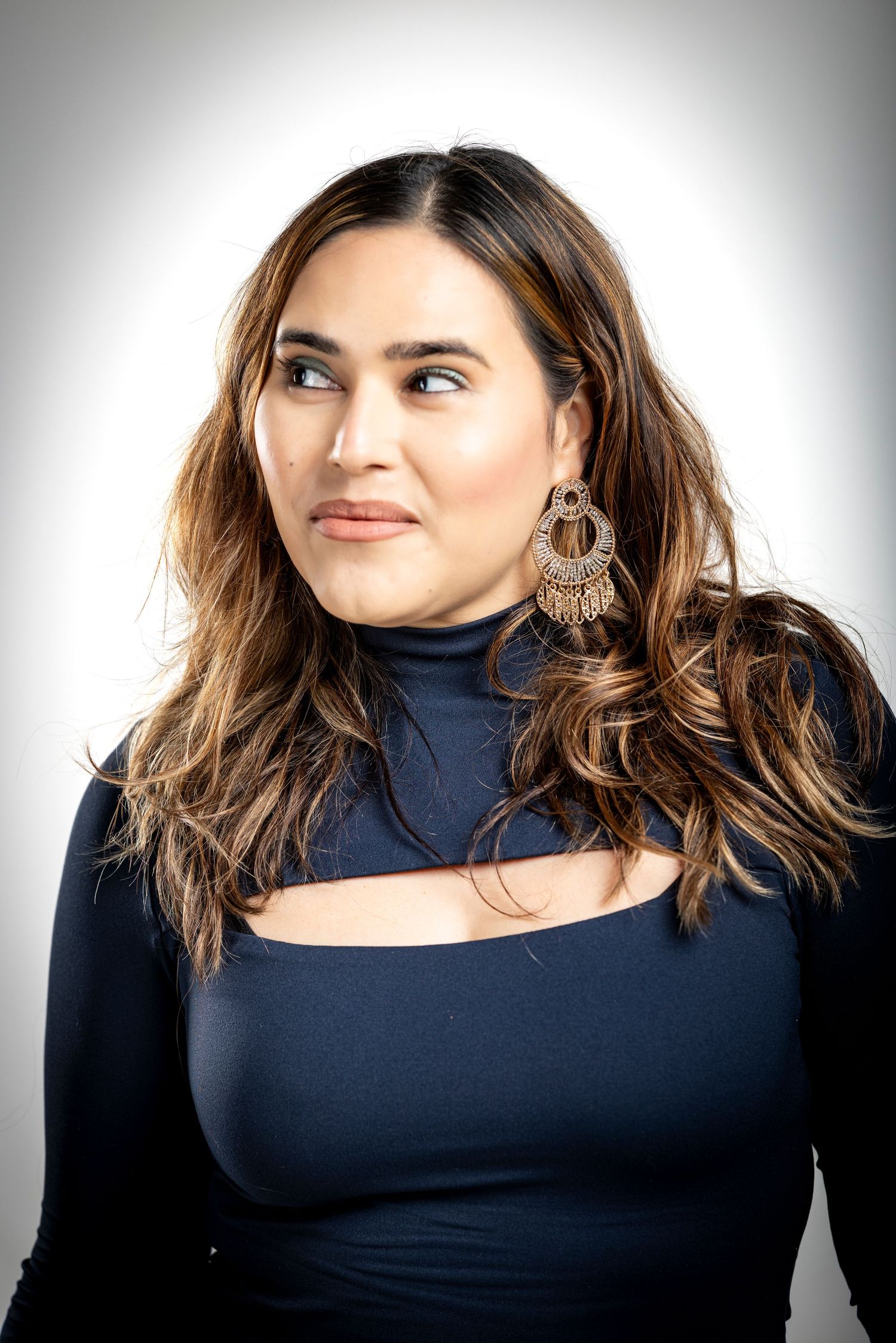 Portrait of a woman in a navy blue cut-out top wearing ornate circular earrings and looking off to the side.