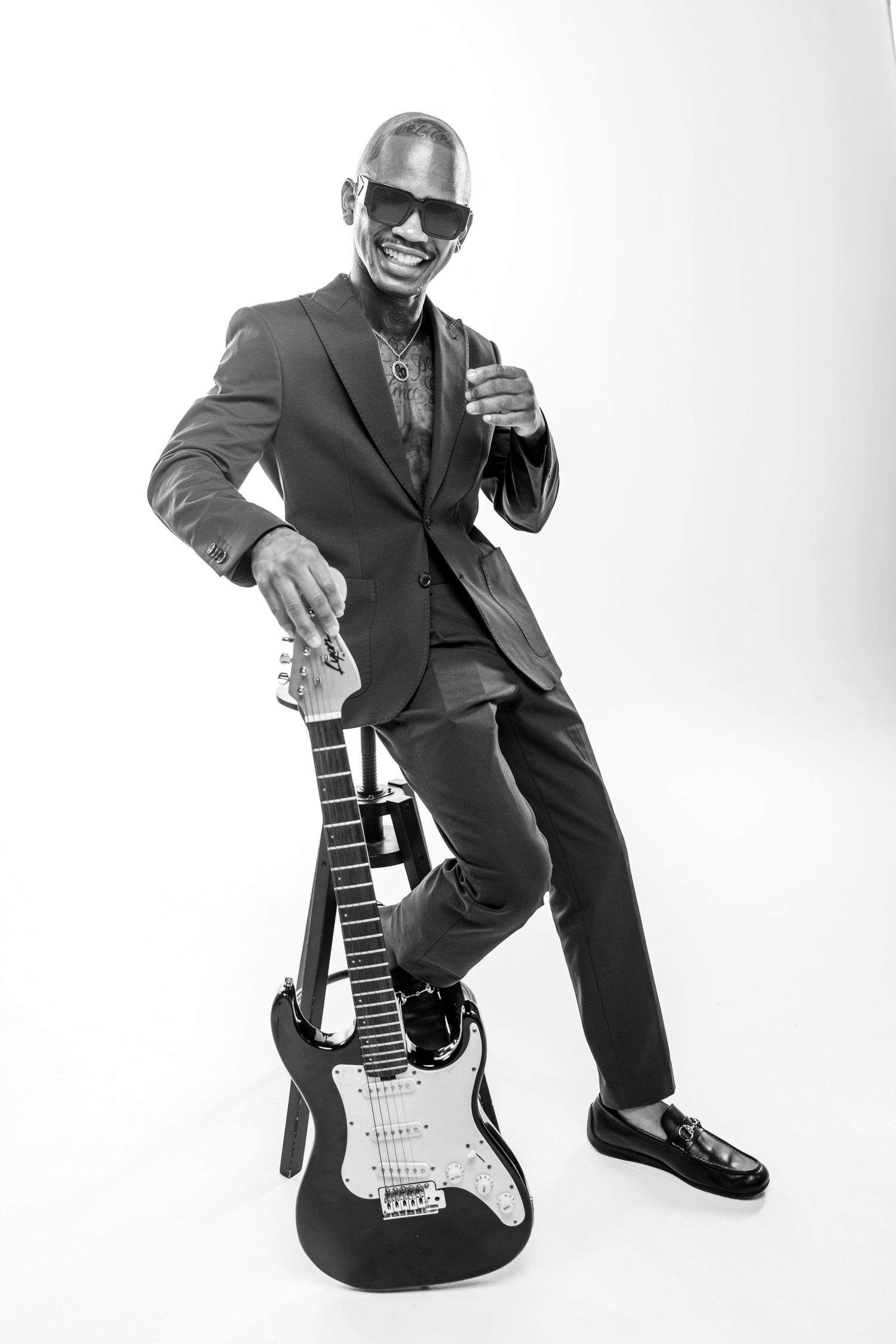Black and white portrait of a musician in a suit posing with an electric guitar and wearing sunglasses.
