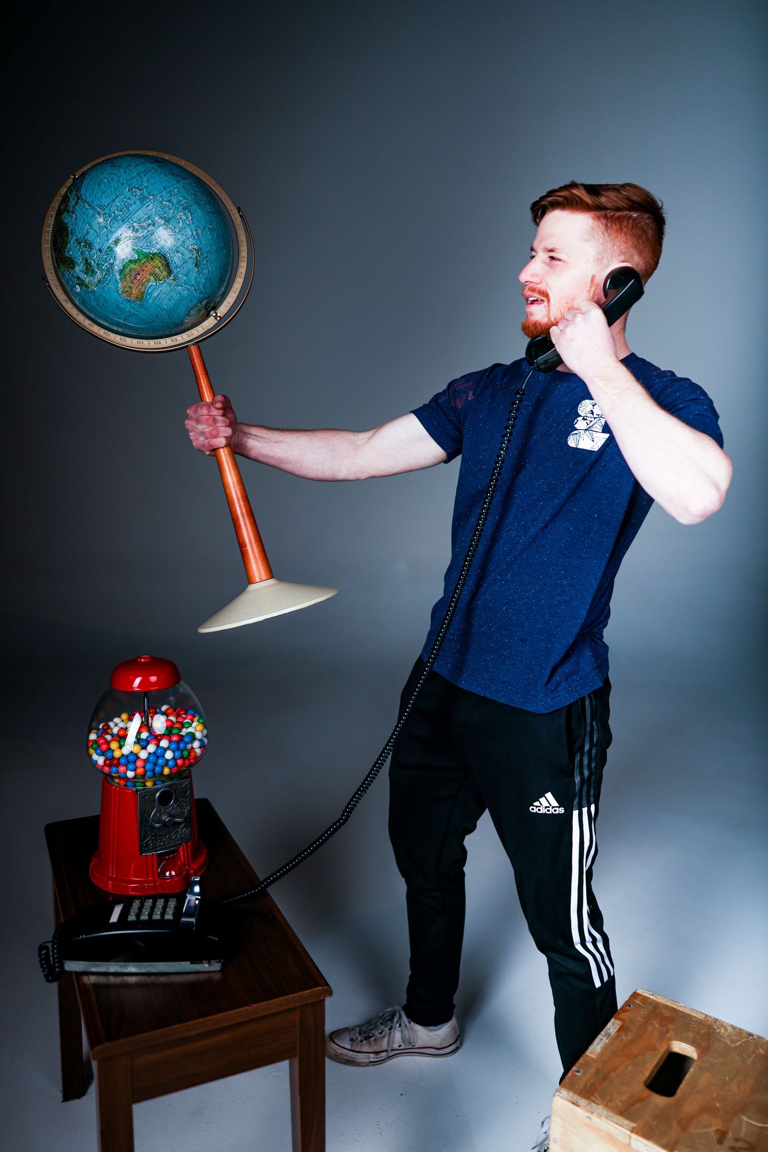 Person holding up a vintage globe table lamp while talking on phone in casual attire against dark background.