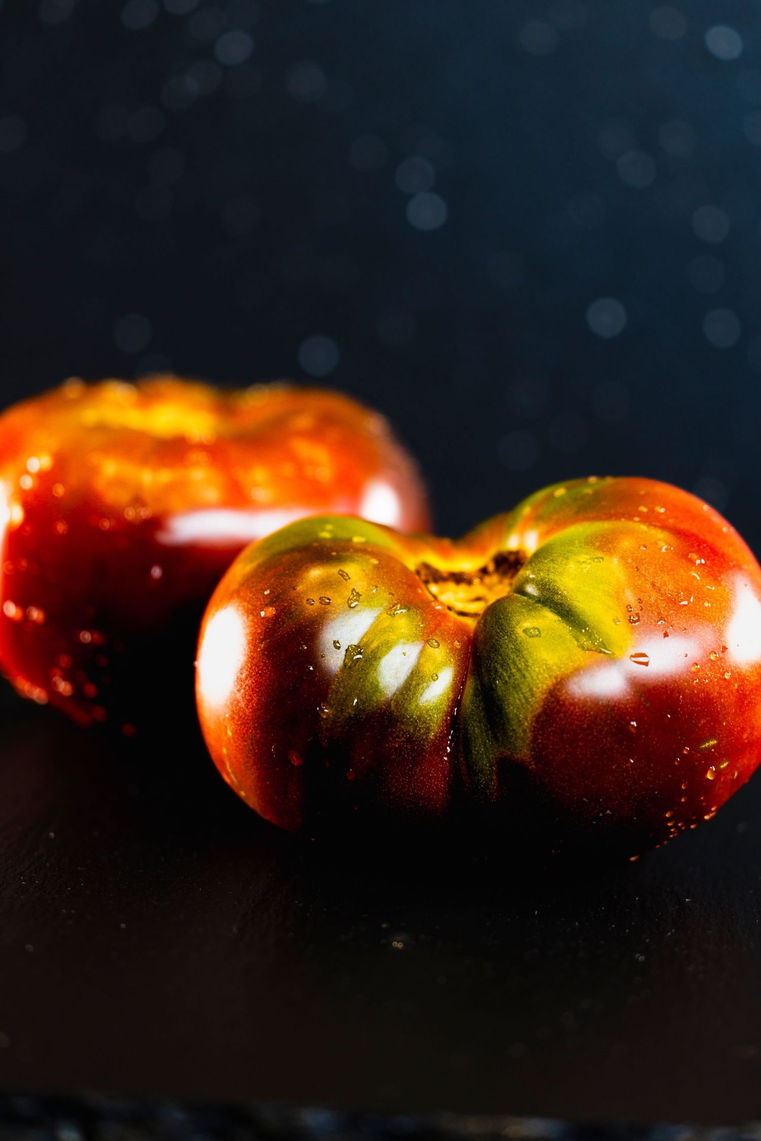 Fresh red and green heirloom tomatoes with water droplets lined up in a dramatic dark lighting setup.