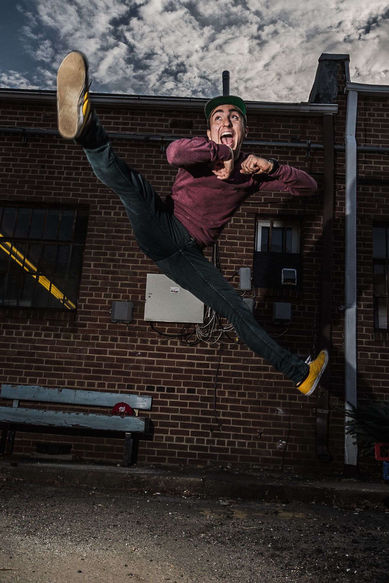 Dramatic street dance move showing a person in burgundy sweater doing an impressive split kick against brick wall at dusk.